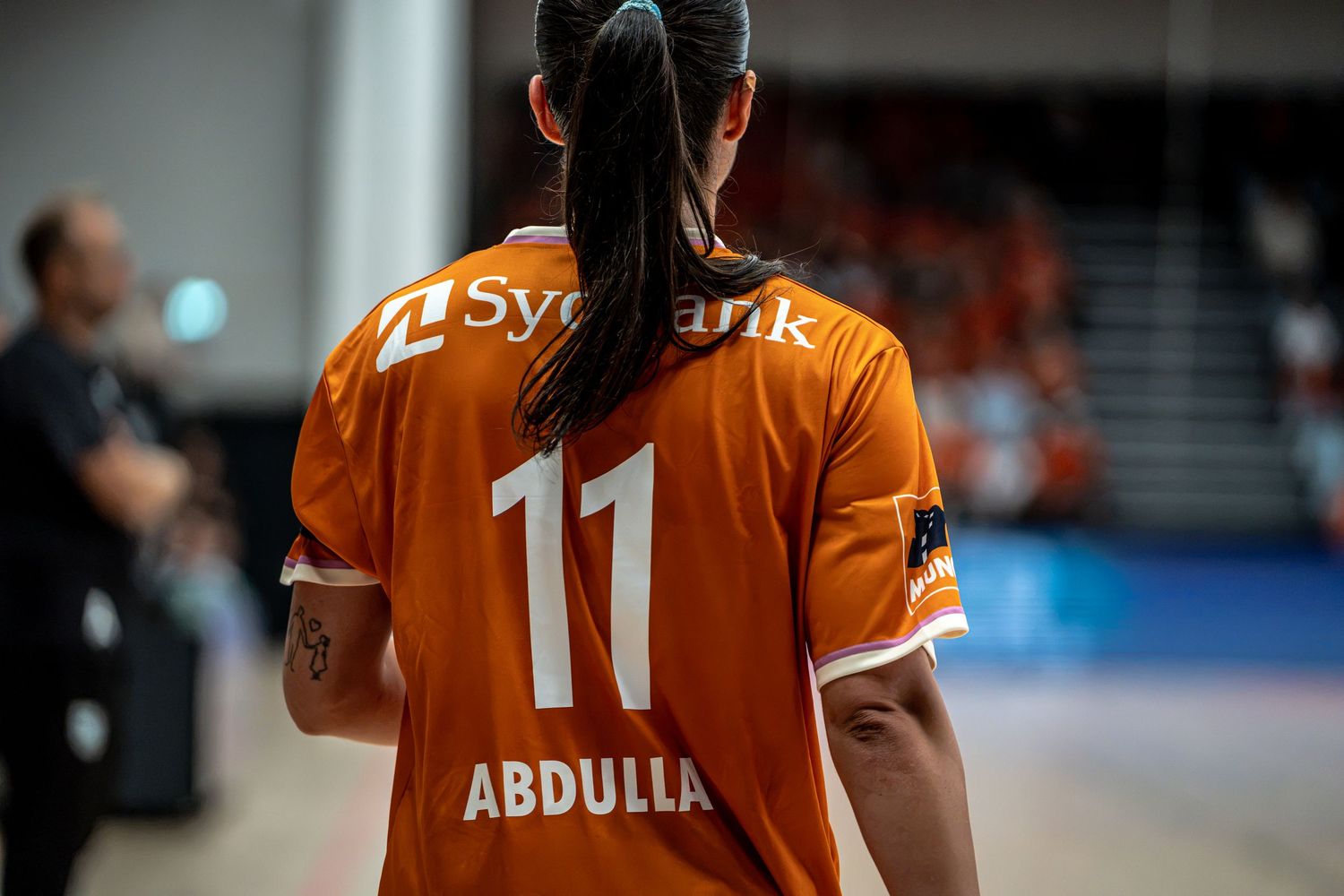 Back view of female handball player wearing orange number 11 Abdulla jersey during indoor match.
