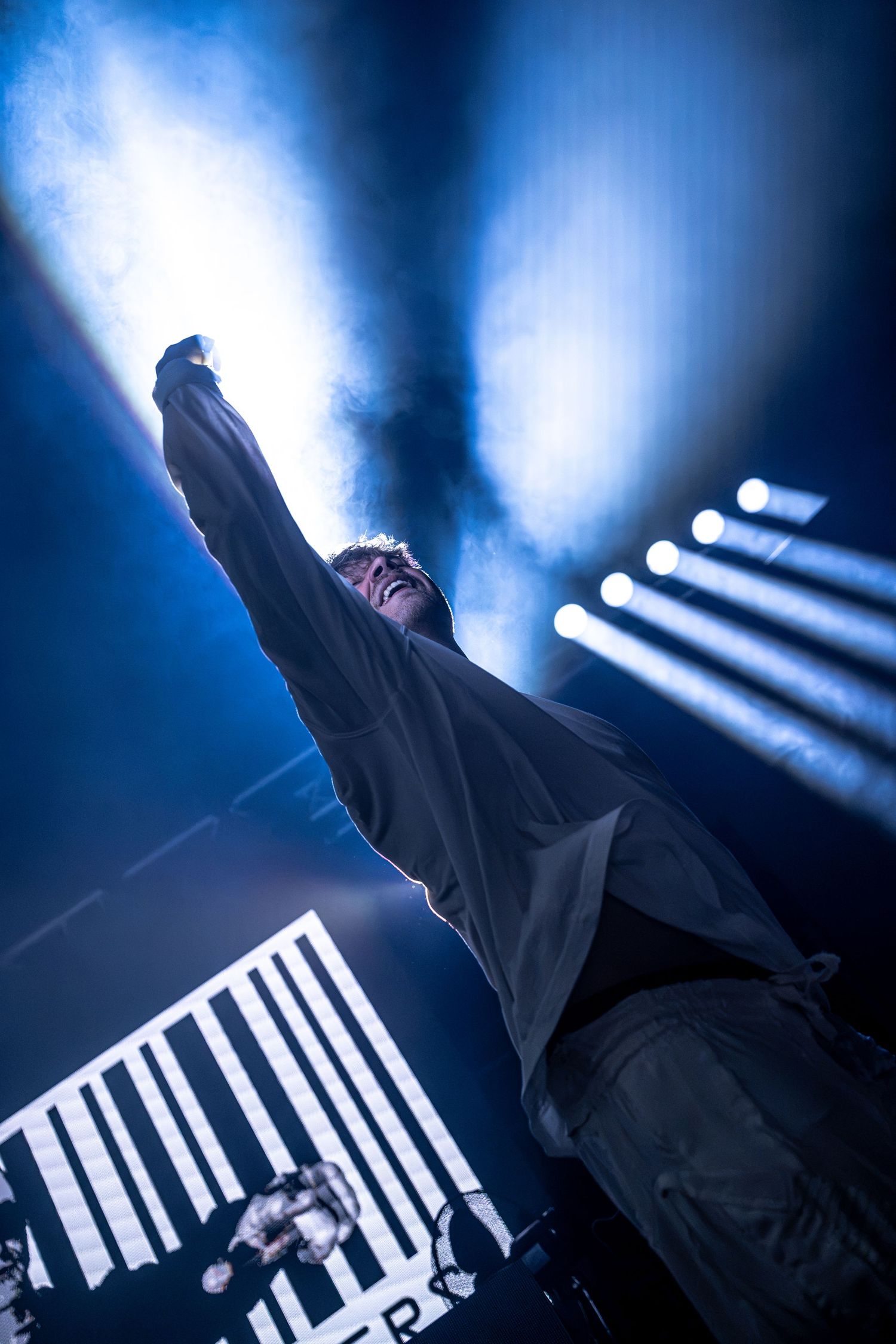 Concert performer raises fist dramatically under blue spotlights on smoky stage.