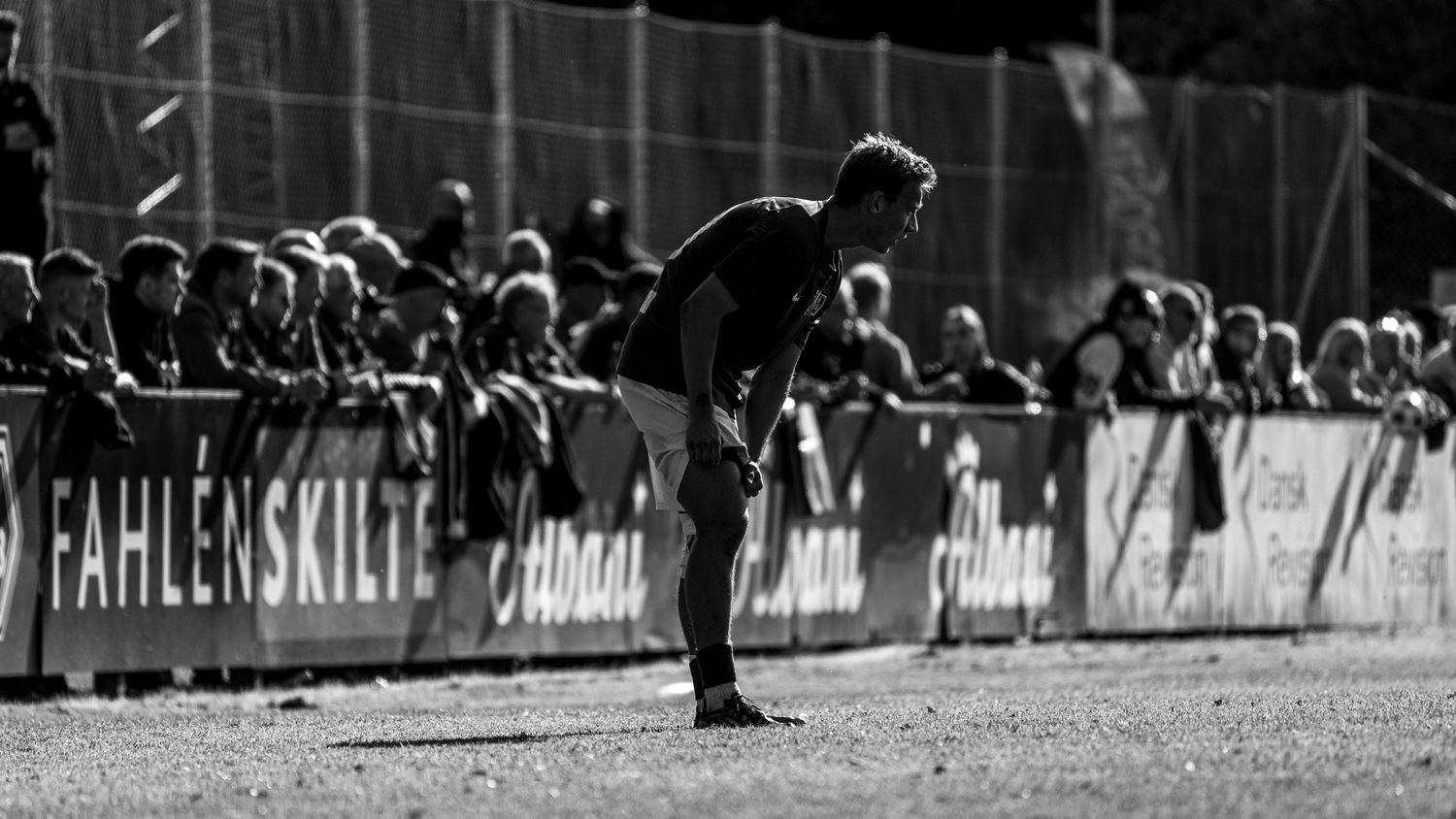 Black and white photo of a soccer player bent over near the sideline before a crowd.