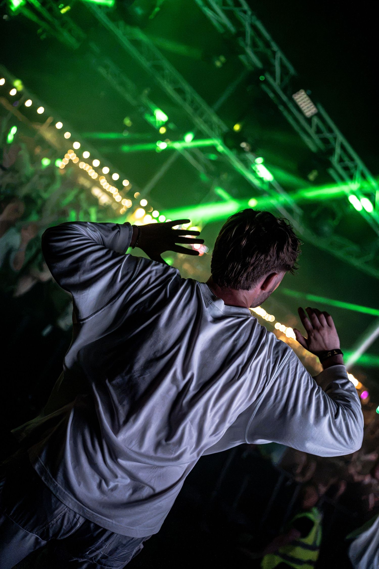 Performer in white hoodie dances with back to crowd under green laser lights at concert.