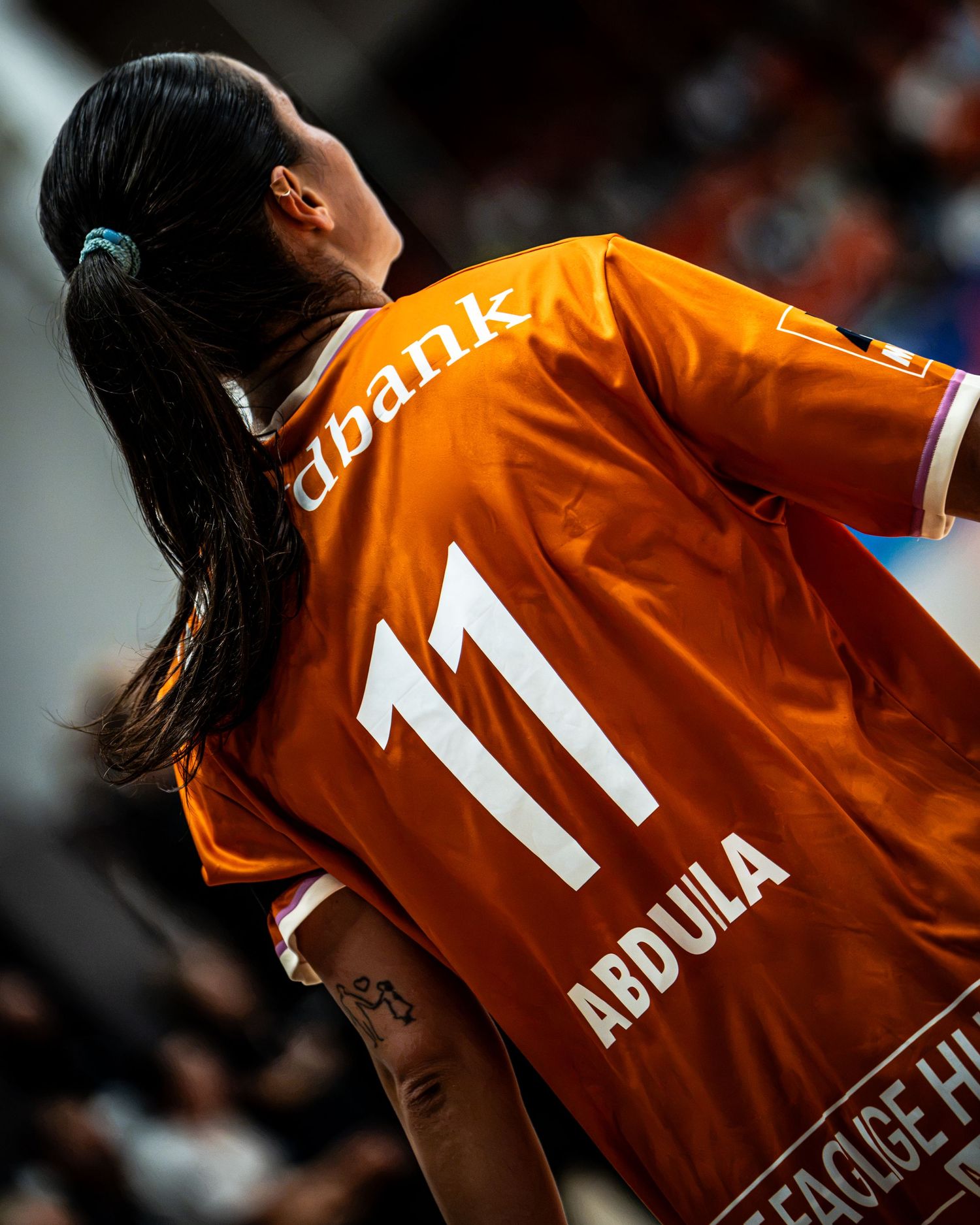 Female handball player wearing orange number 11 jersey with name Abdula on the back during a match.