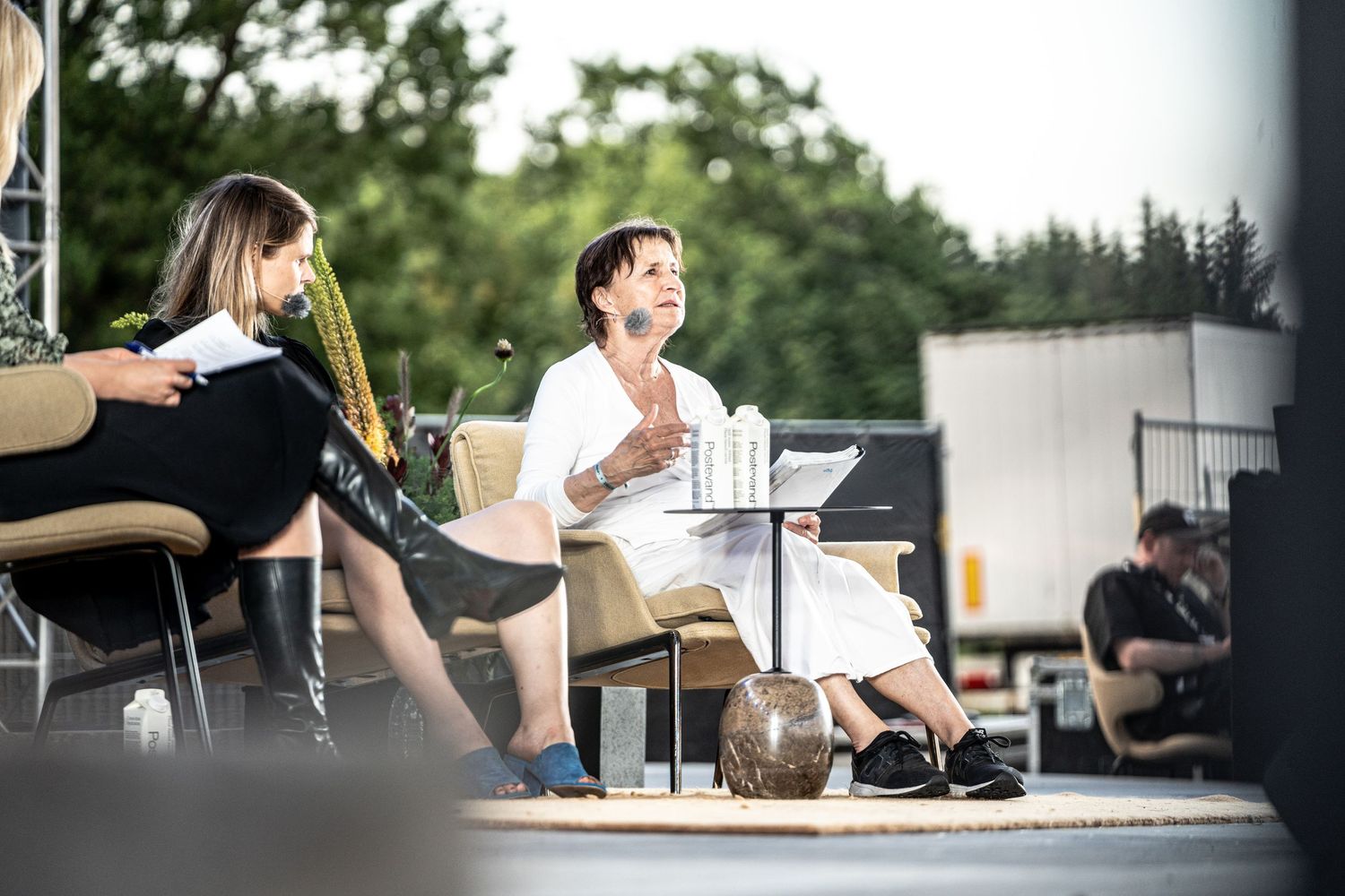 Two women seated on an outdoor stage during a panel discussion at an open-air event.
