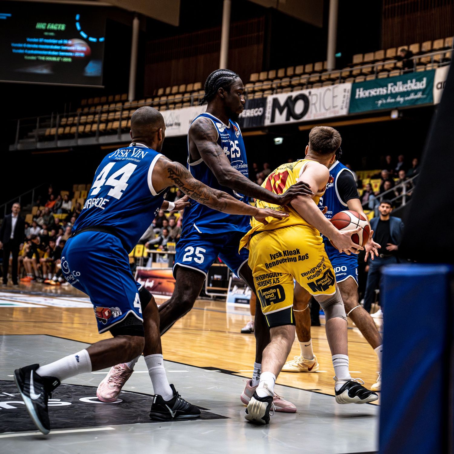 Blue and yellow basketball players compete in an intense game at a professional Danish basketball arena.