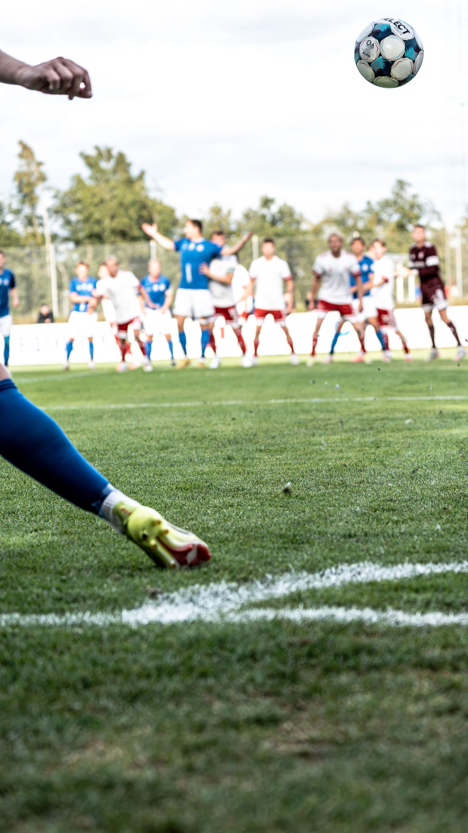 Soccer player taking a free kick with teammates and opponents forming a wall in background.