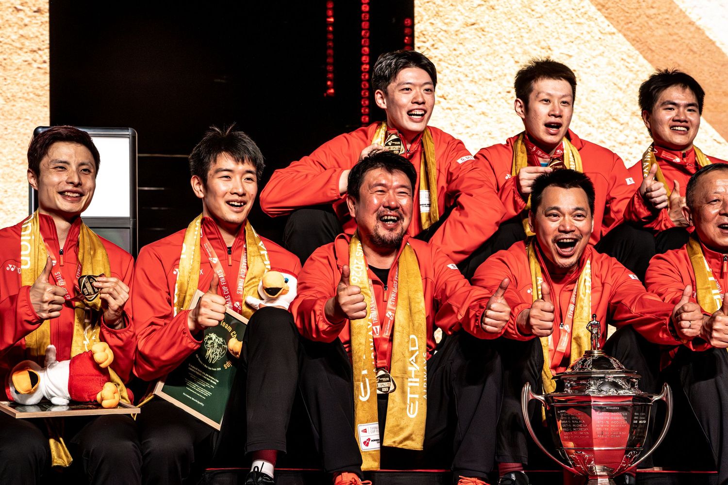 Team China players and coaches celebrate joyfully with medals after winning badminton championship.