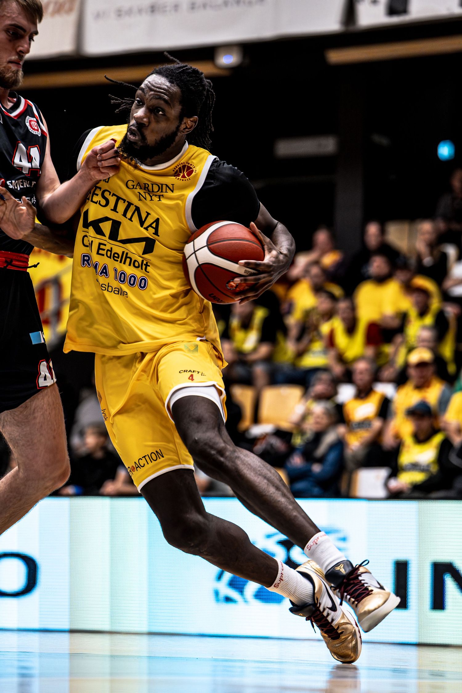 Dynamic action shot of yellow jersey basketball player driving past defender in crowded arena.