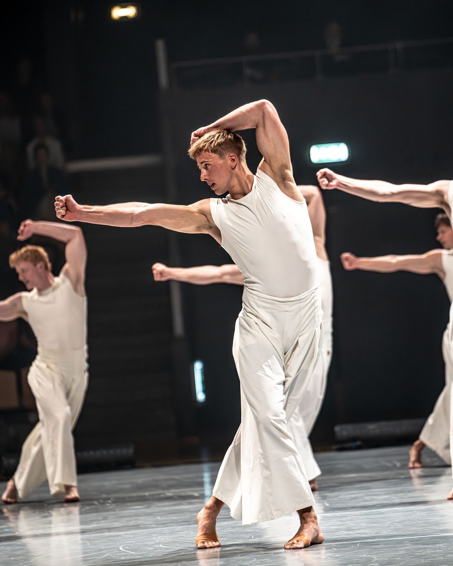 Male contemporary dancer in white costume performs expressive arm movement on stage.