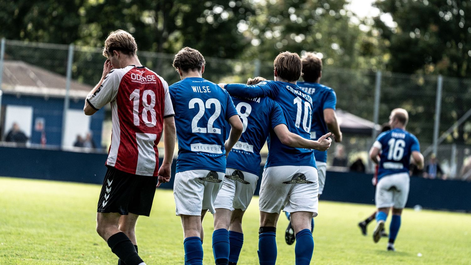 Soccer players in blue jerseys celebrate together after scoring during an outdoor match.