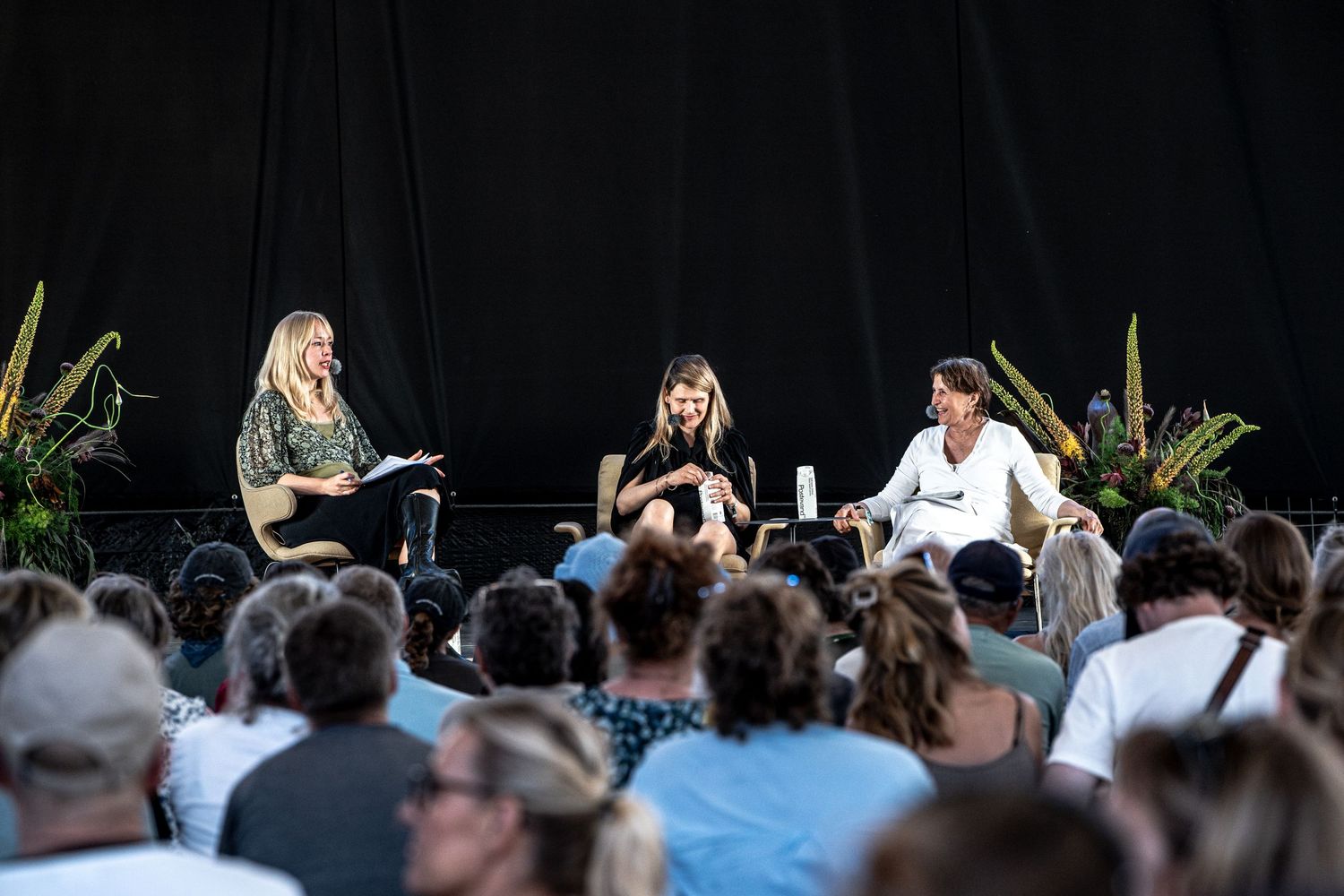 Panel of three women presenting to seated crowd at outdoor event.