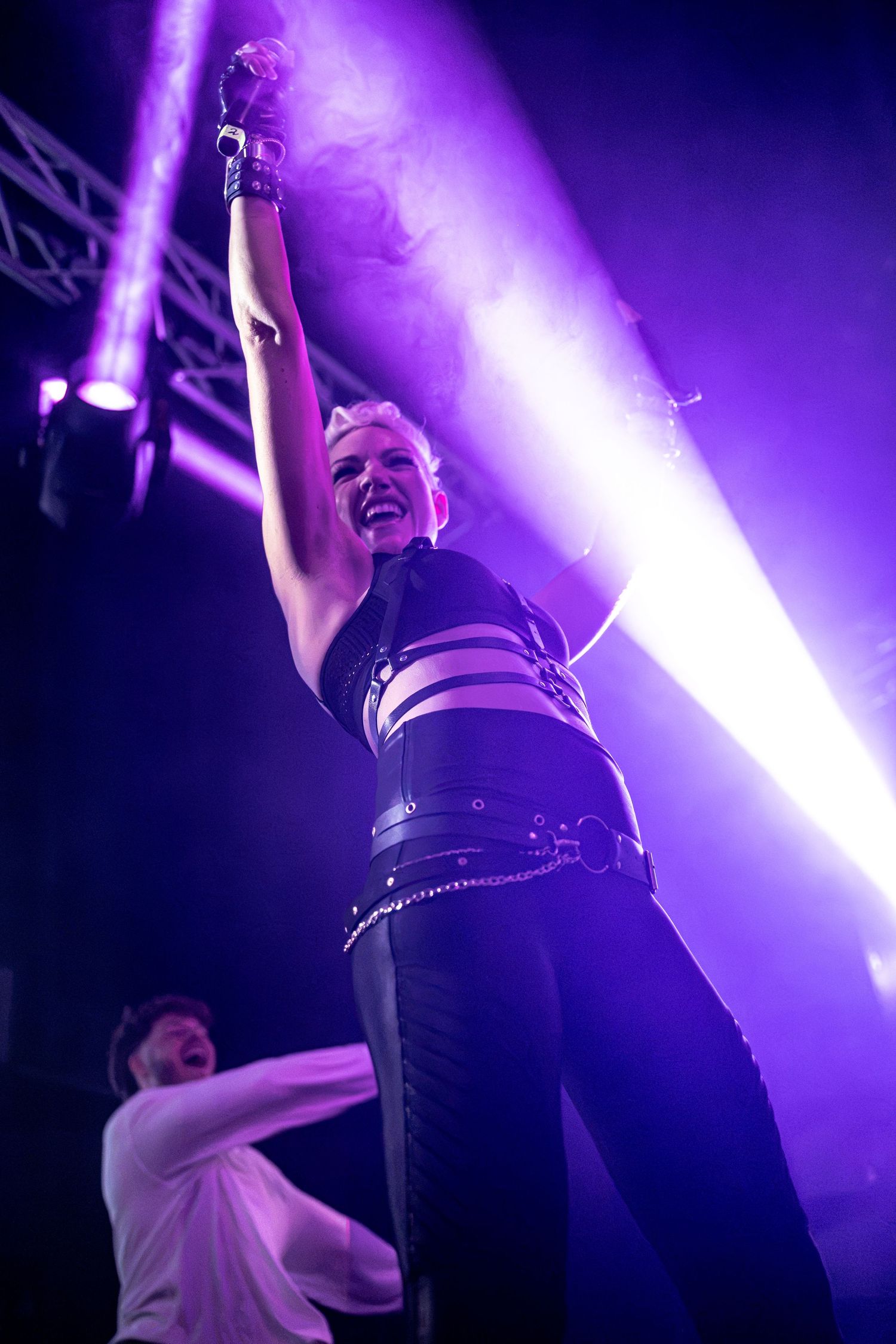 Female performer raises arm triumphantly on stage bathed in purple concert lighting.