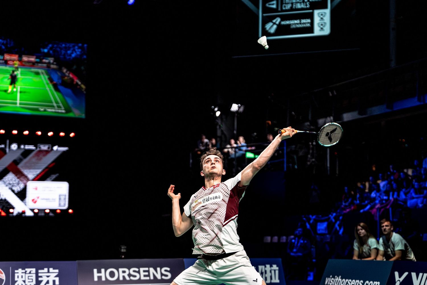 Badminton player jumping to smash shuttlecock at Horsens indoor arena during professional tournament.