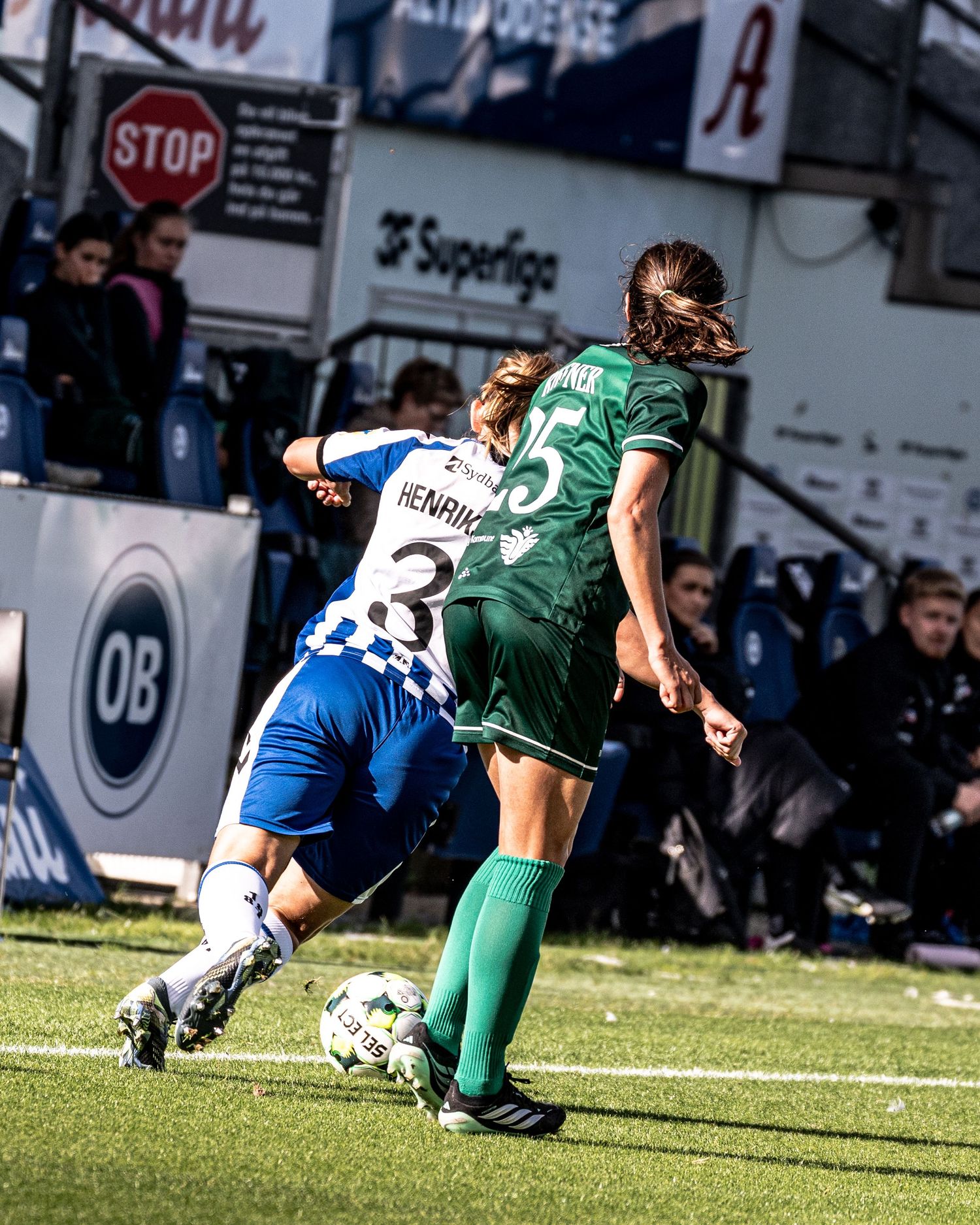 Female soccer players battle for the ball during a competitive women's football match at OB stadium.