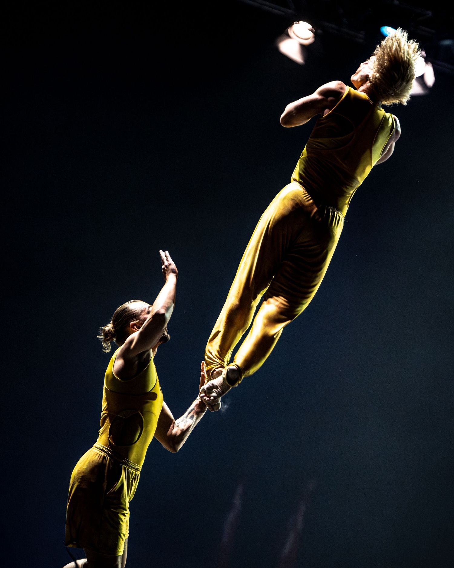 Two acrobats in yellow costumes performing a breathtaking aerial lift during a professional circus performance.
