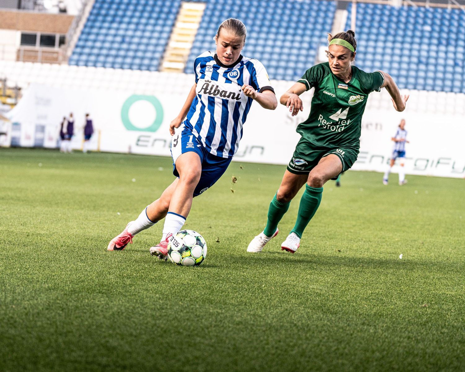 Female soccer players compete for the ball during a match between blue-white and green-uniformed teams.