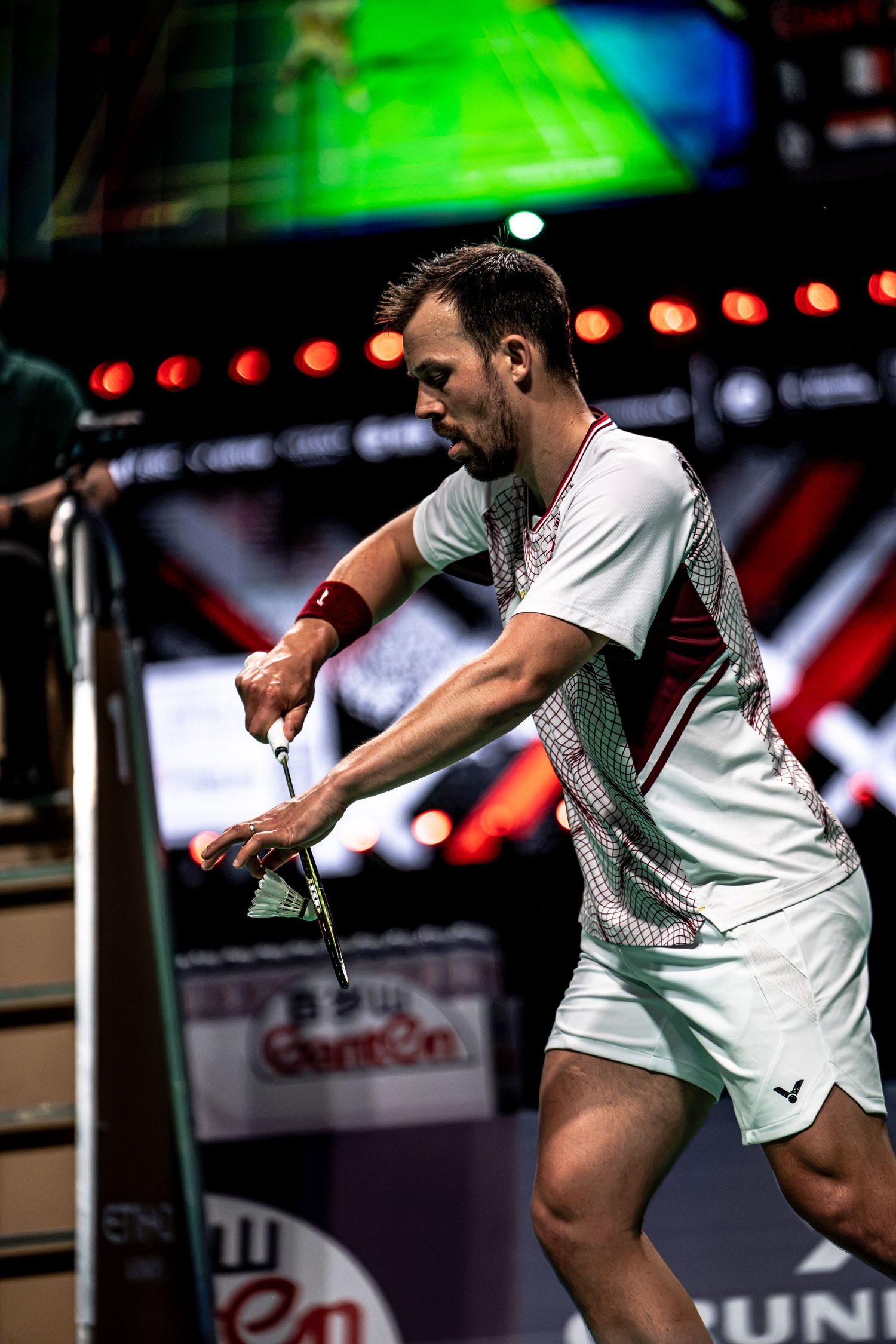 Professional badminton player in white Victor uniform preparing to serve shuttlecock during BWF Thomas Cup Finals.