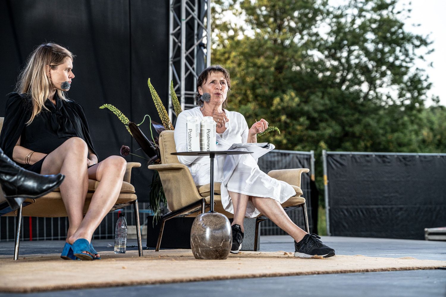Two women seated on an outdoor stage engaged in a calm panel discussion.