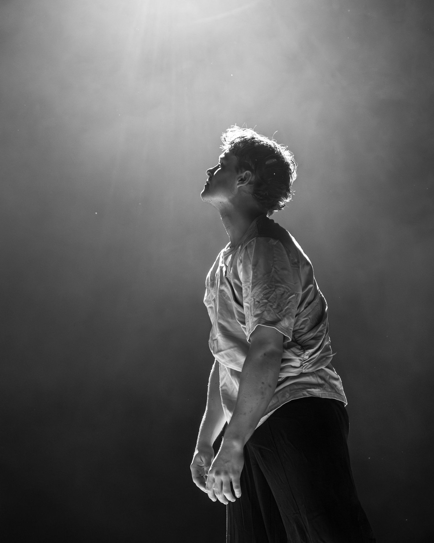 Dancer stands in dramatic spotlight with head tilted back in black and white stage photo.