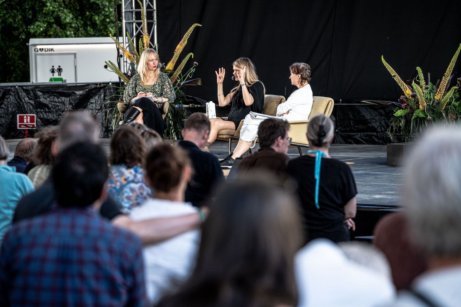 Three women on stage in panel discussion at outdoor festival event.