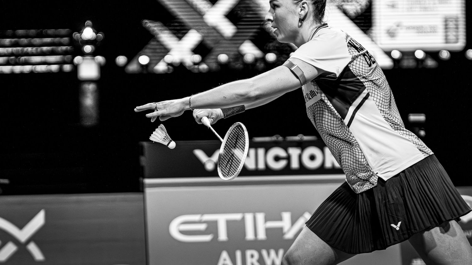 Black and white photo of female badminton player preparing to serve during an Etihad Airways sponsored match.