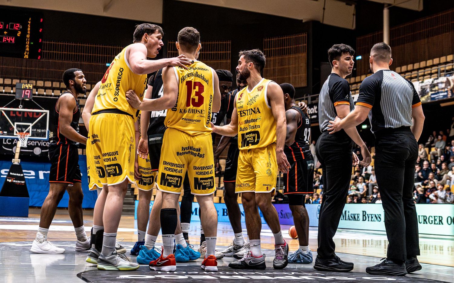 Yellow-uniformed basketball team huddles with coaches during a timeout on the court.