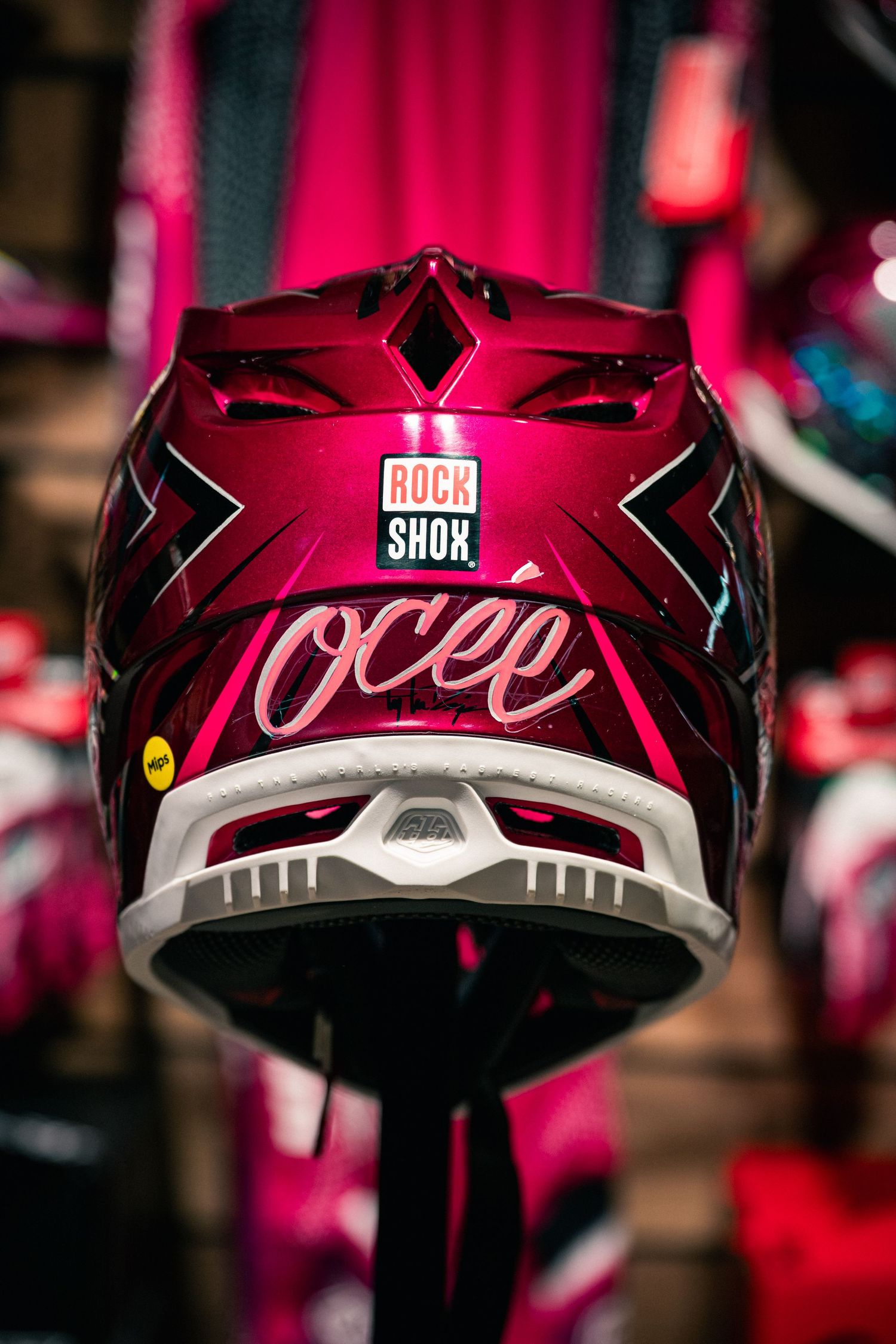A glossy crimson motorcycle helmet with Rock Shox sticker and Ocee branding displayed on a stand.