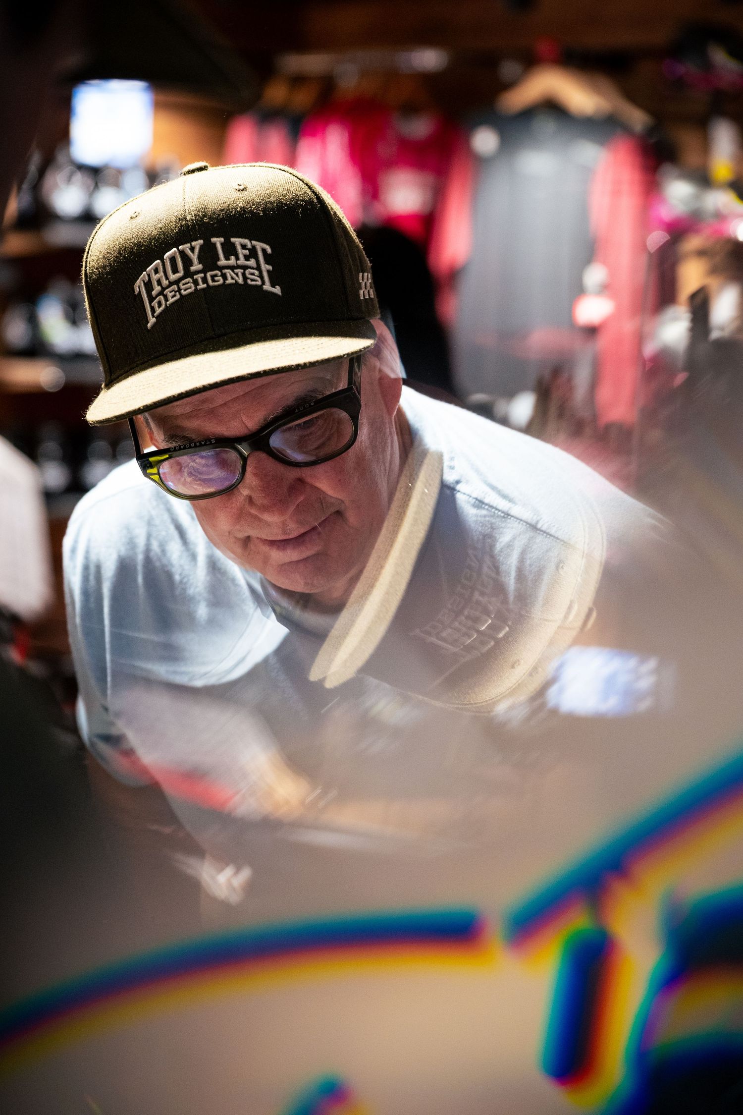 Man wearing Troy Lee Designs cap and glasses working intently in a colorful shop.