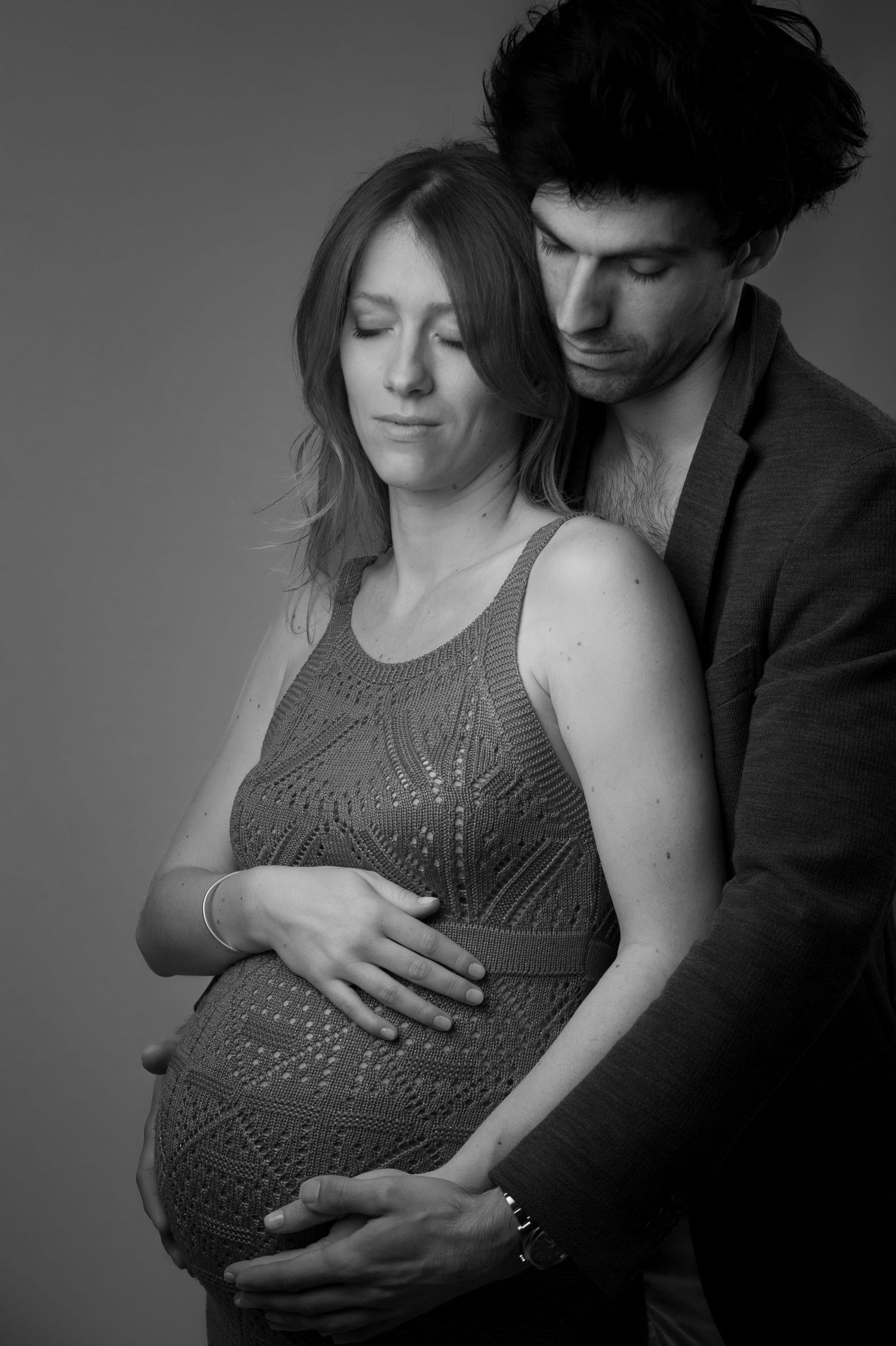 Black and white portrait of a couple embracing, with the man holding the womans pregnant belly.