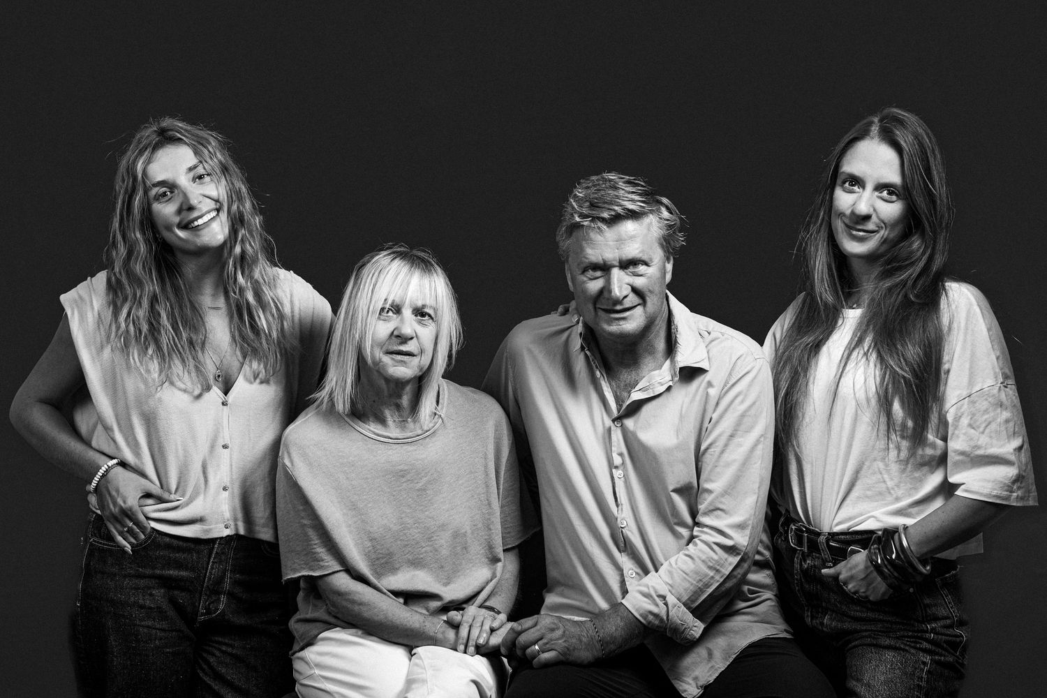 Black and white portrait of four smiling people, two older adults and two young women, posing together on dark background.