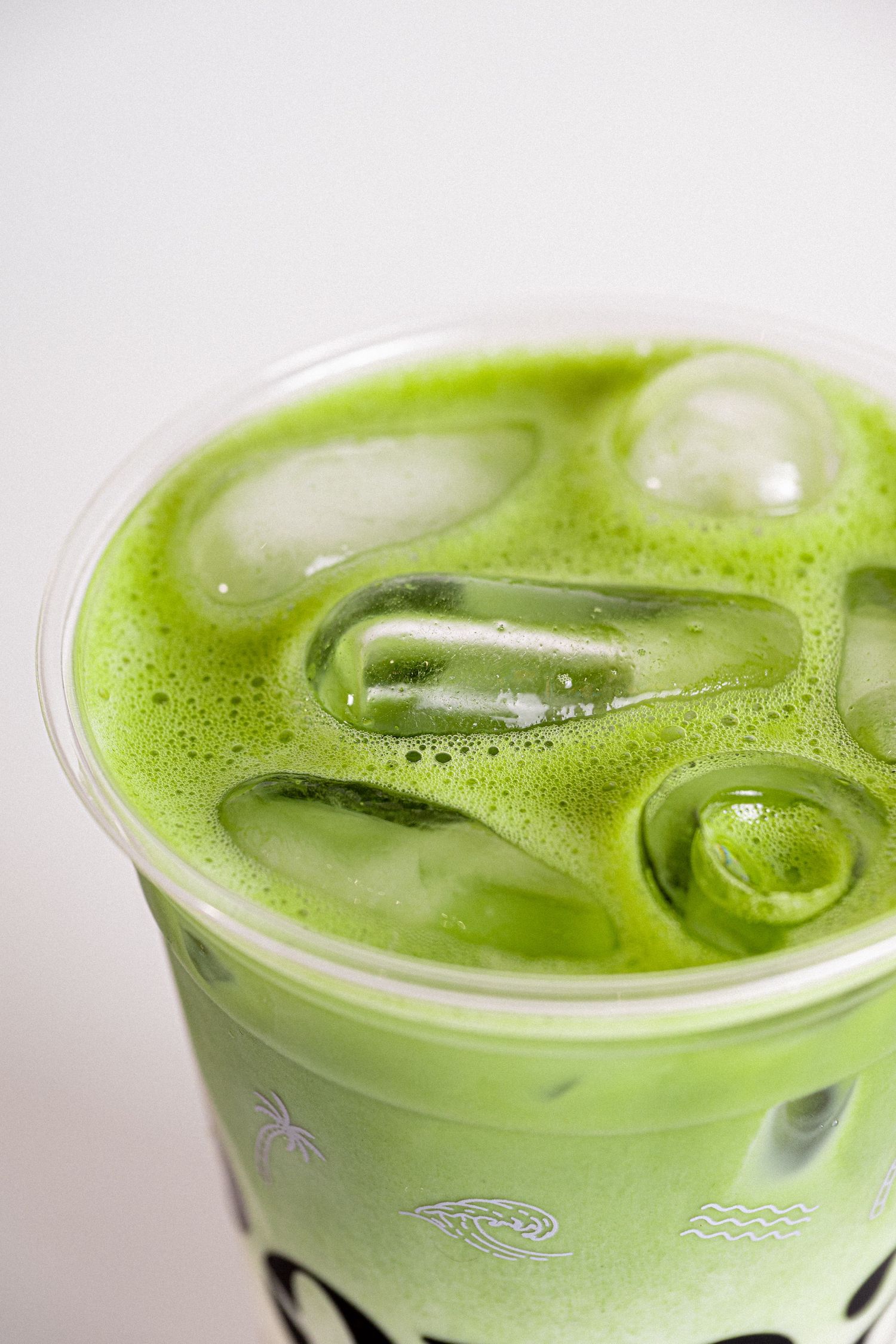 Close-up of an iced matcha green tea latte in a clear plastic cup with ice cubes.