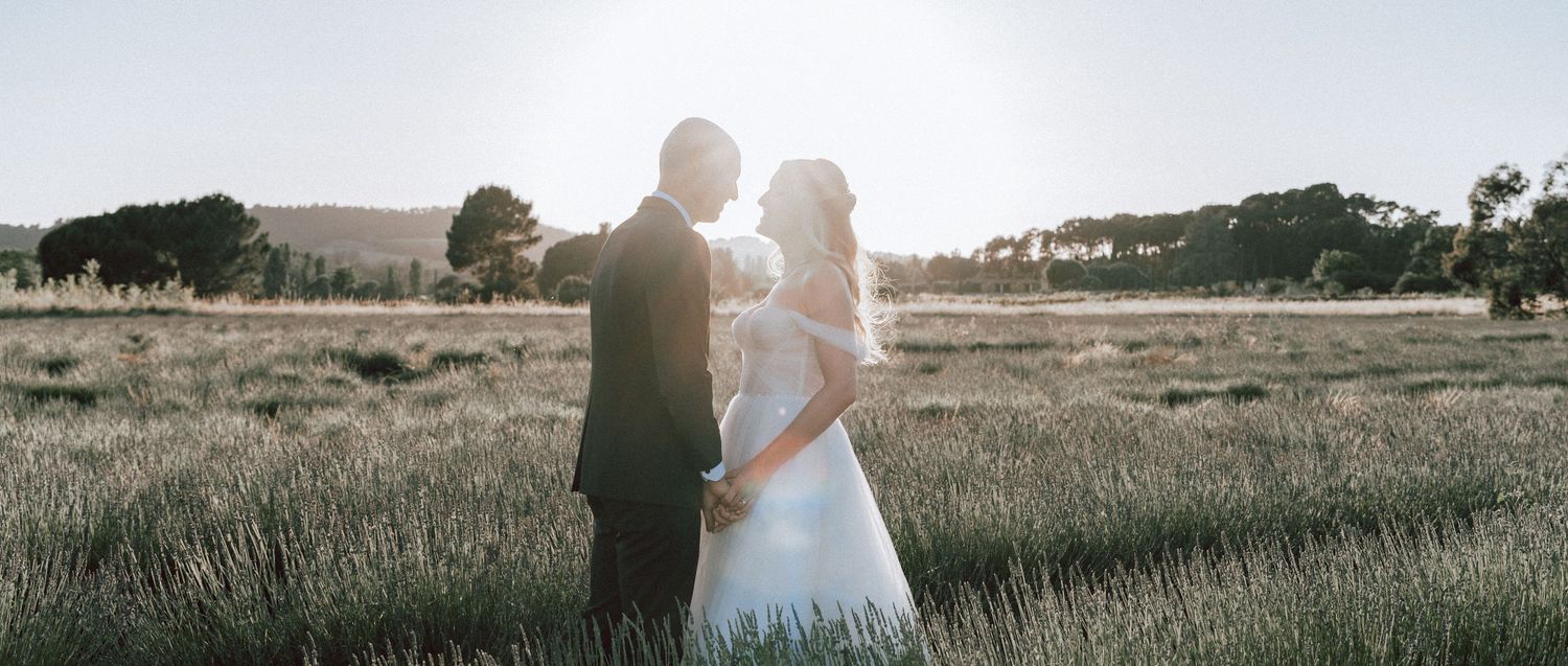 Bride and groom standing together in golden sunlit field during romantic outdoor wedding portrait session.