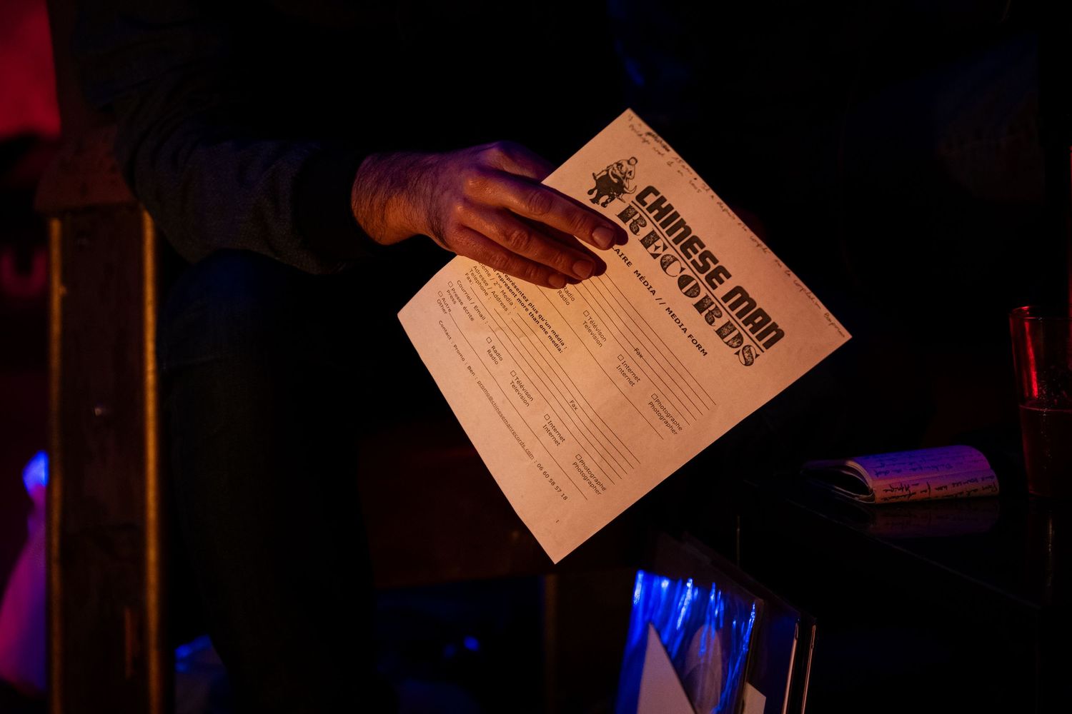 Person holding a Morse Man event flyer in a dimly lit venue with blue accent lighting.