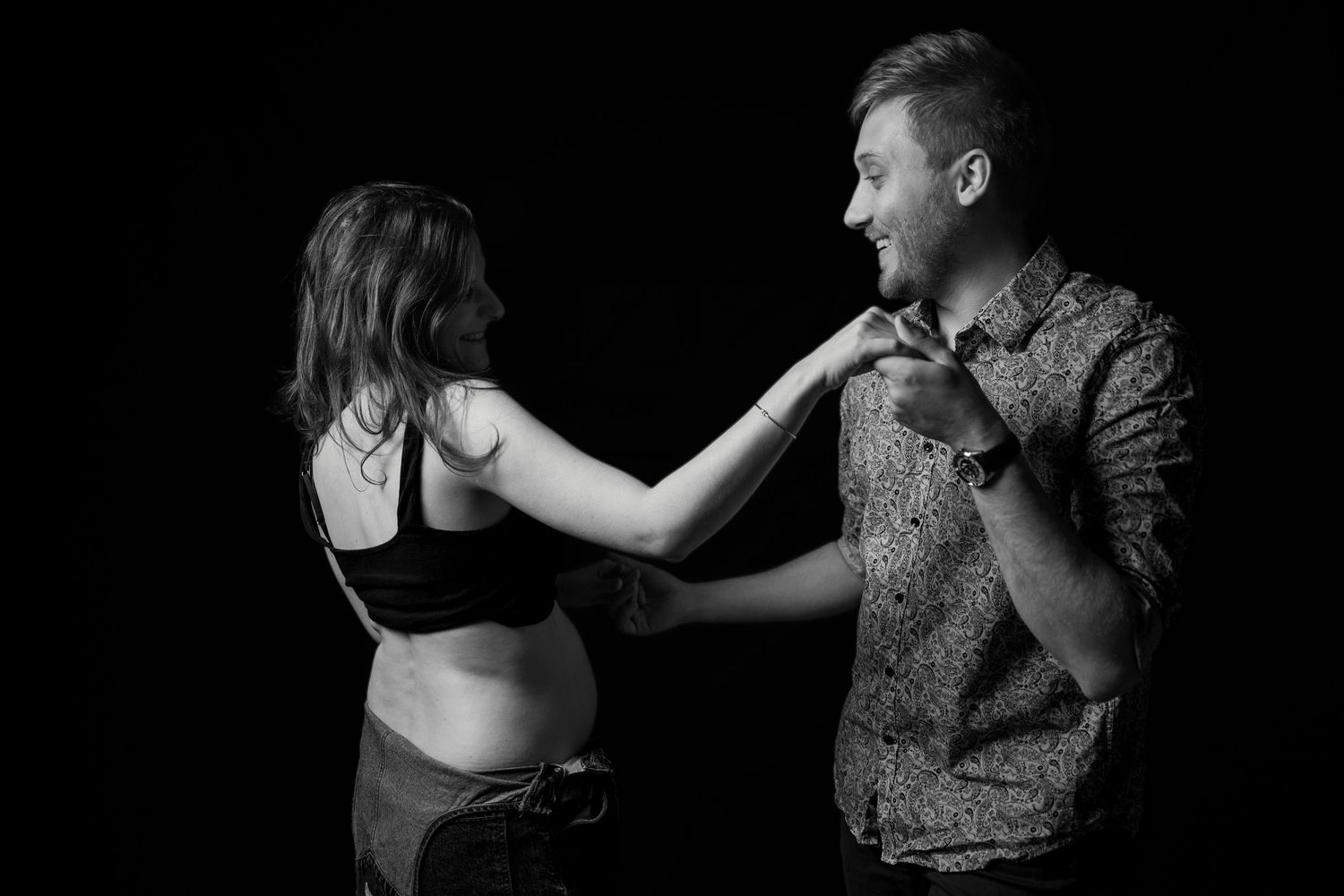 Pregnant woman and man sharing a playful moment together in black and white studio maternity photo.