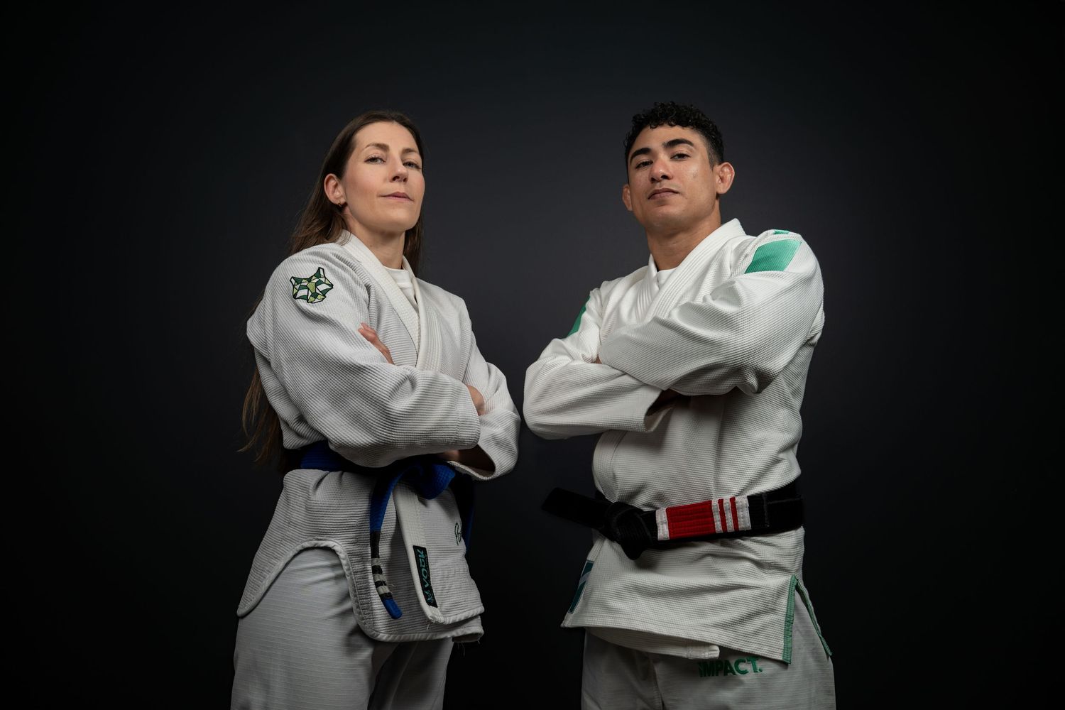 Two judo athletes in white gi uniforms standing with arms crossed against a dark background.