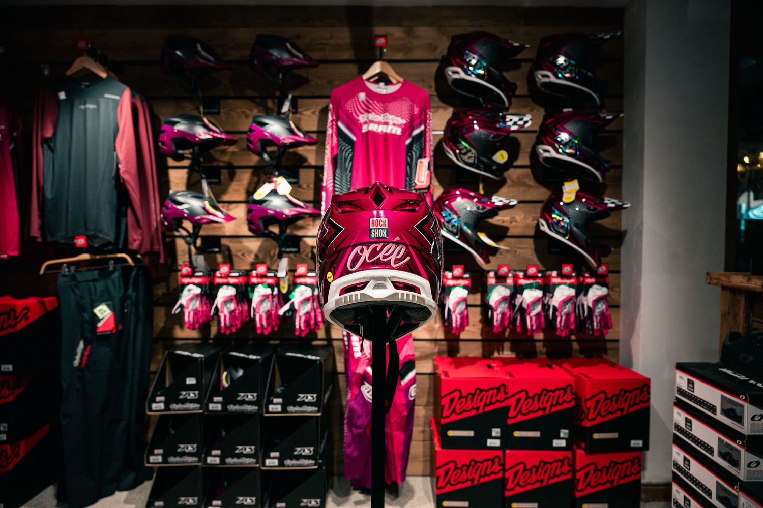 Pink motocross gear display featuring helmets, jerseys, gloves, and pants arranged on a retail store wall.