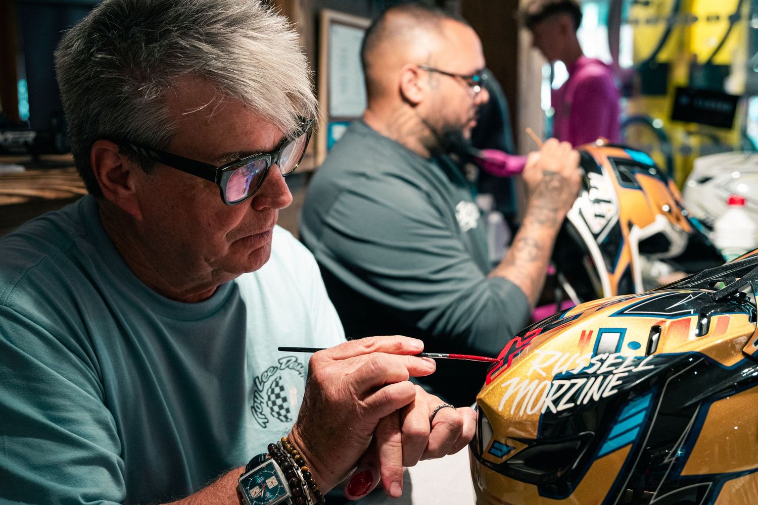 Artist using a fine brush to paint custom designs on a motocross helmet in a workshop.