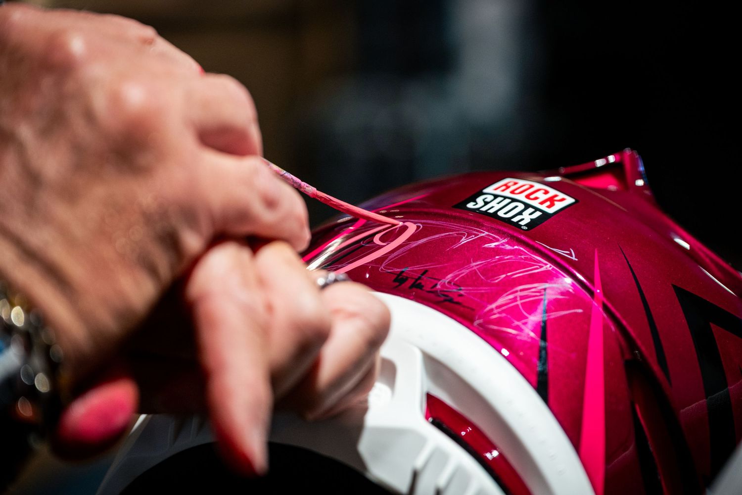 Hands adjusting a vibrant pink RockShox branded helmet with metallic swirl design details.