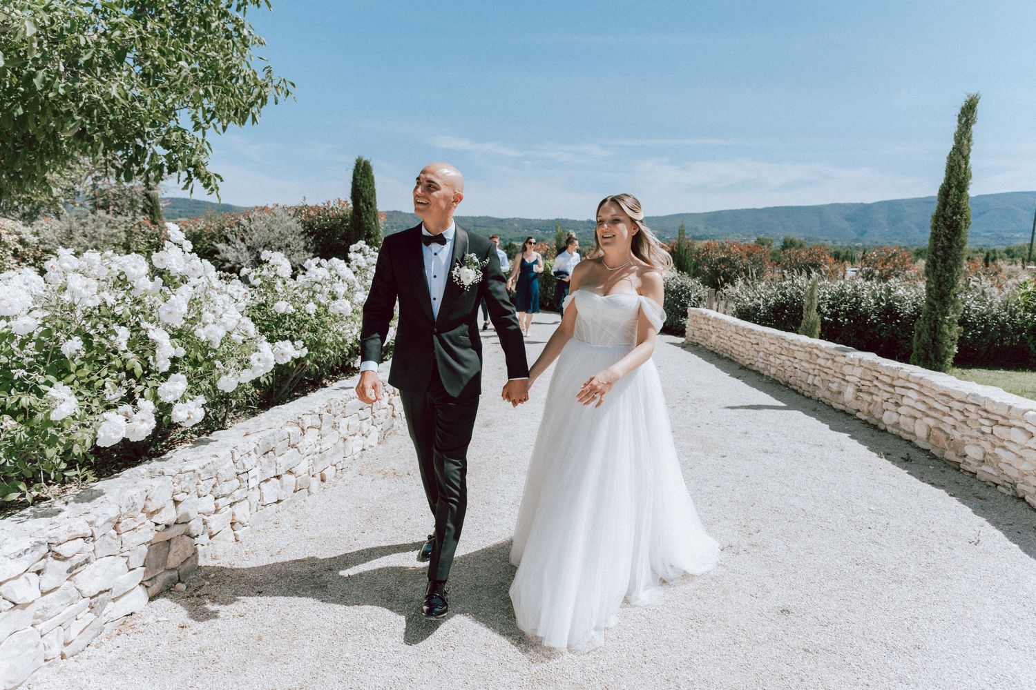 Bride and groom walking hand in hand through scenic garden path on wedding day.