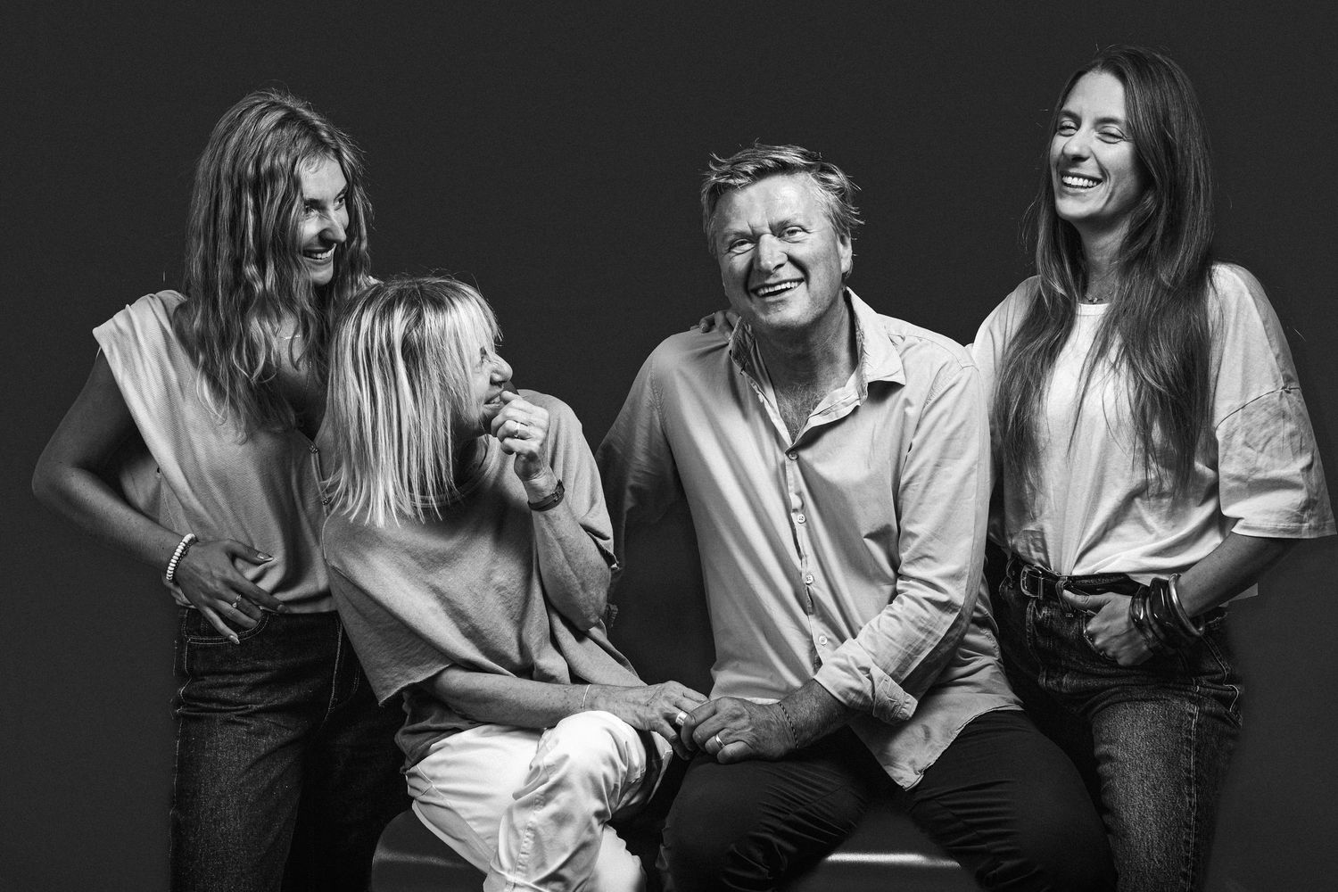 Happy family of four laughing together in black and white studio portrait photo.