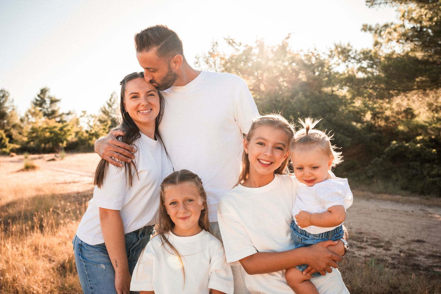 Happy family of five in white shirts posing outdoors in golden sunlit field.