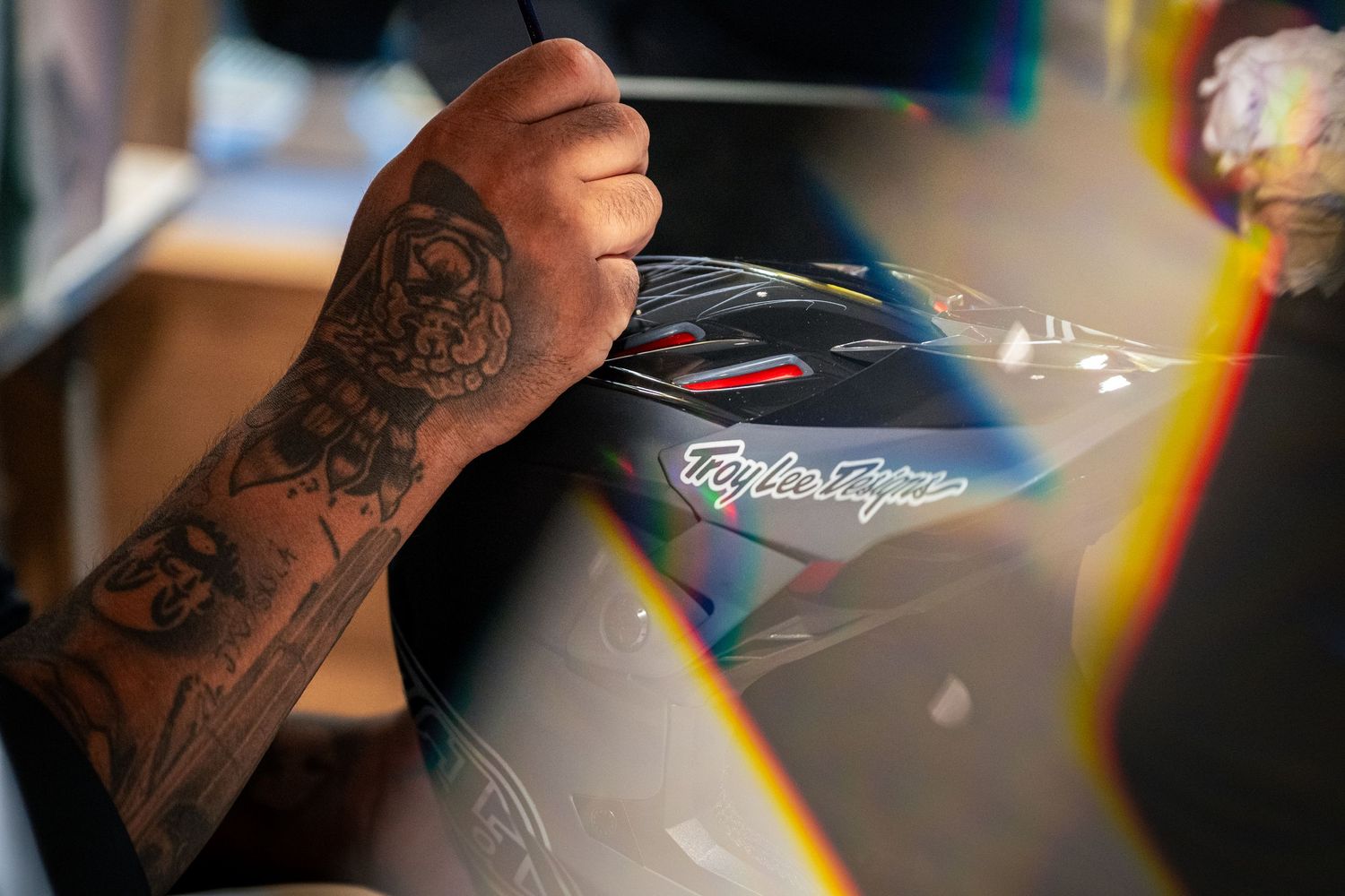 Tattooed hand signing a Troy Lee Designs helmet, close-up detail shot.