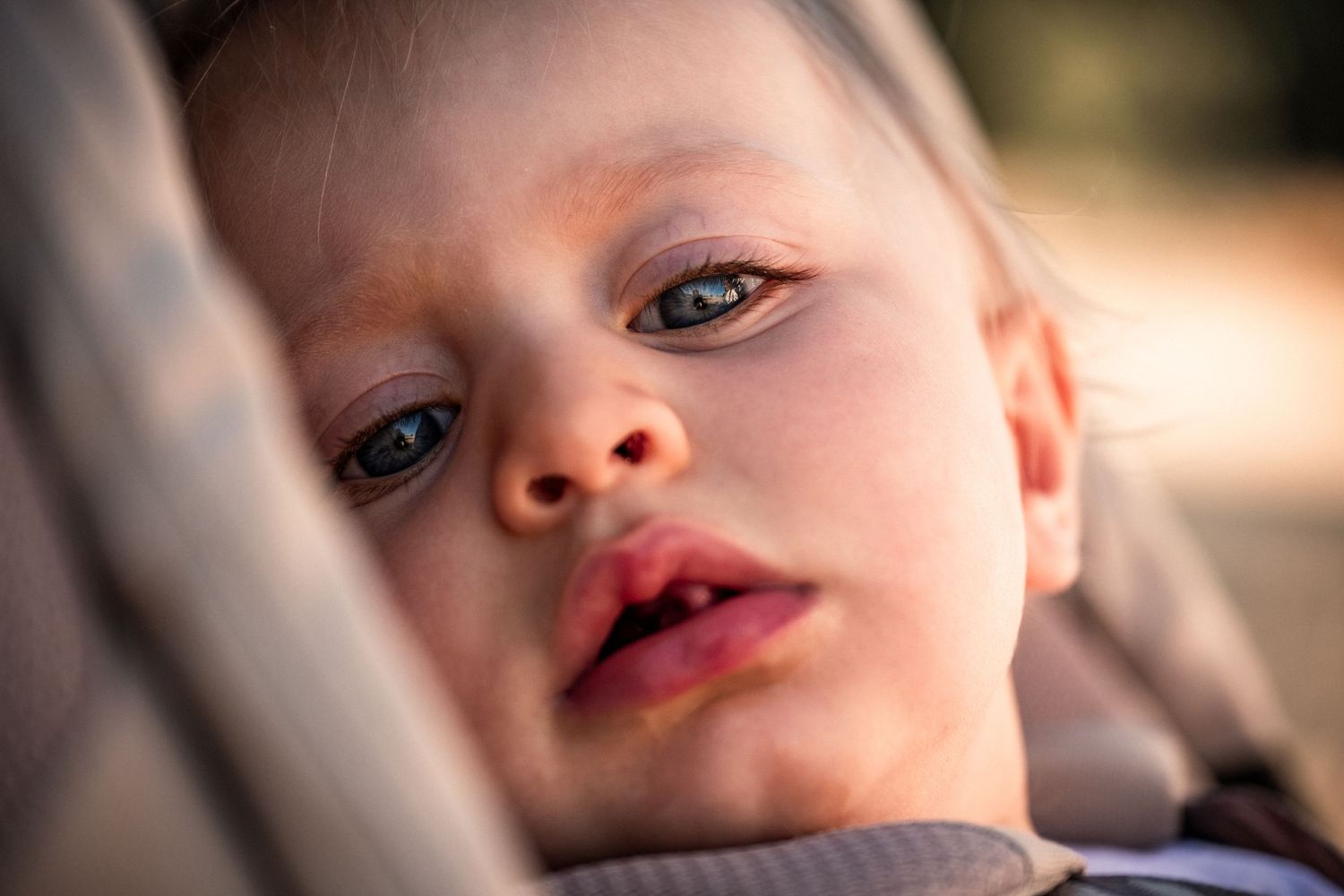 Close-up portrait of a sleepy blue-eyed toddler resting in a stroller seat.
