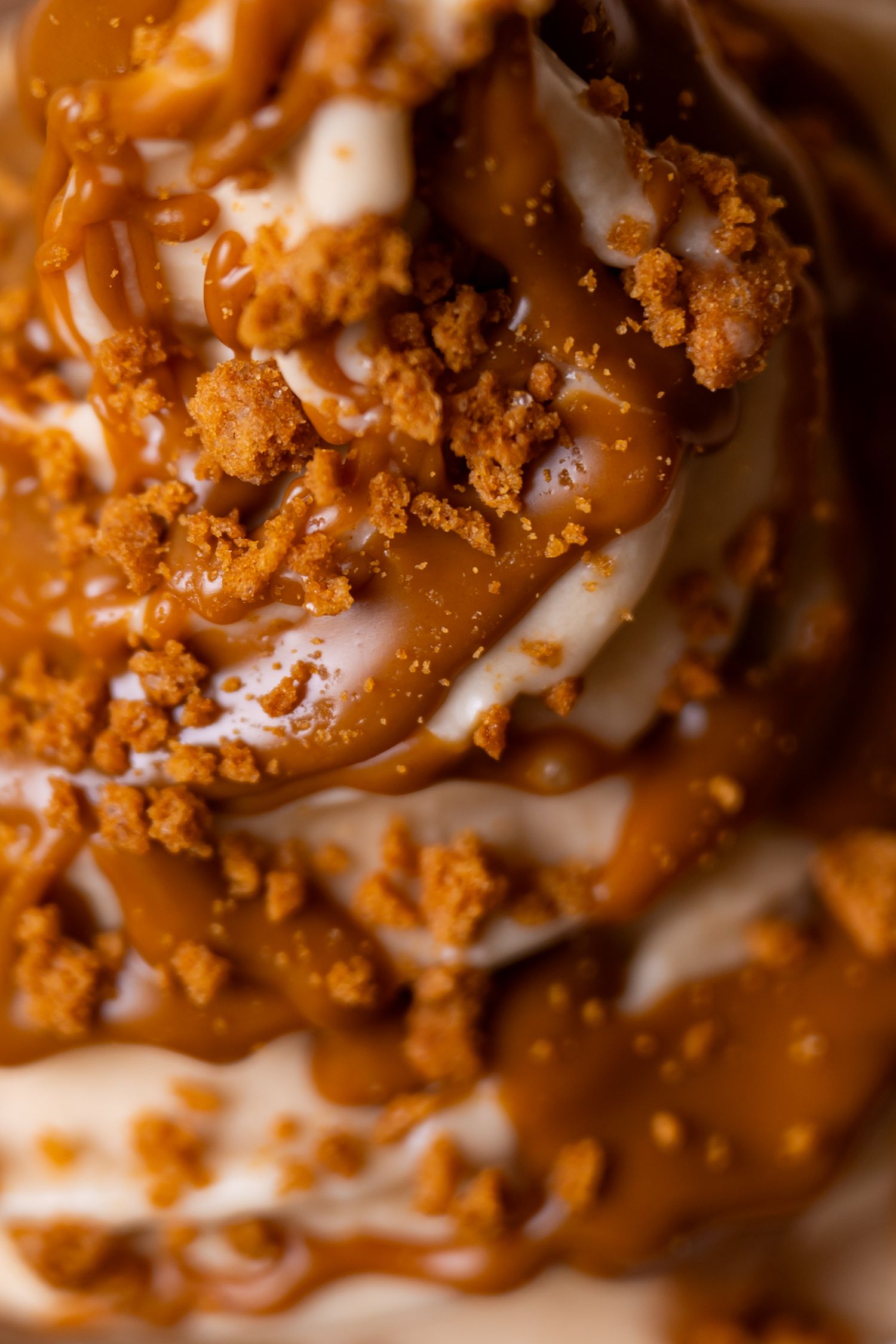 Close-up of vanilla ice cream topped with caramel sauce and golden cookie crumbles.