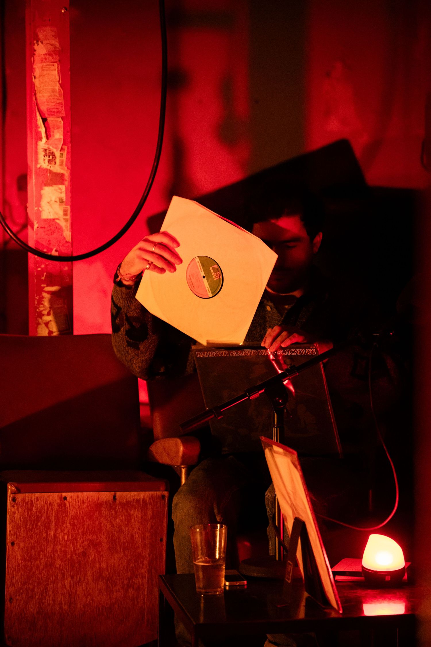 DJ holding vinyl record in red-lit atmospheric venue during a music performance.