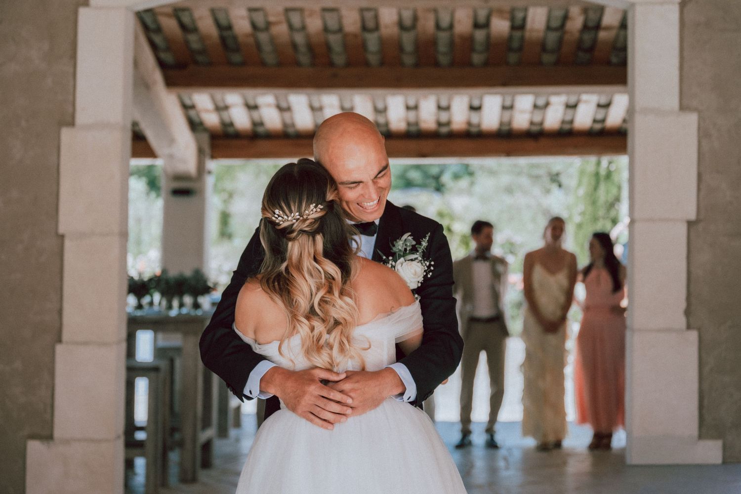 Bride and groom share first dance embrace at outdoor wedding venue with guests watching in background.