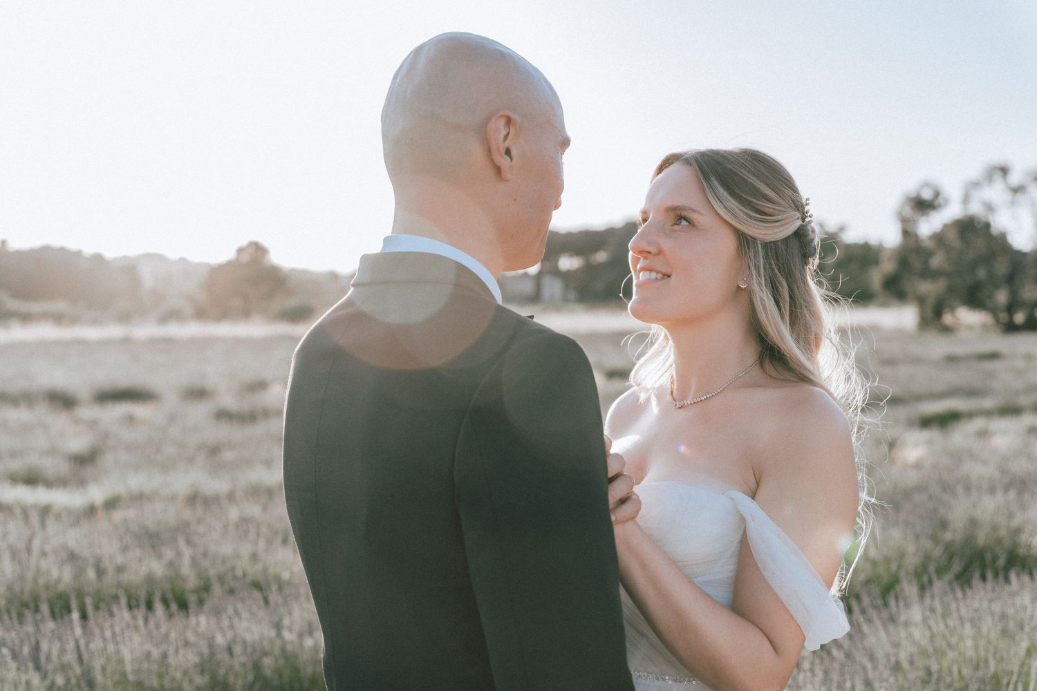 Bride smiles up at groom during golden hour portrait in an open field on their wedding day.