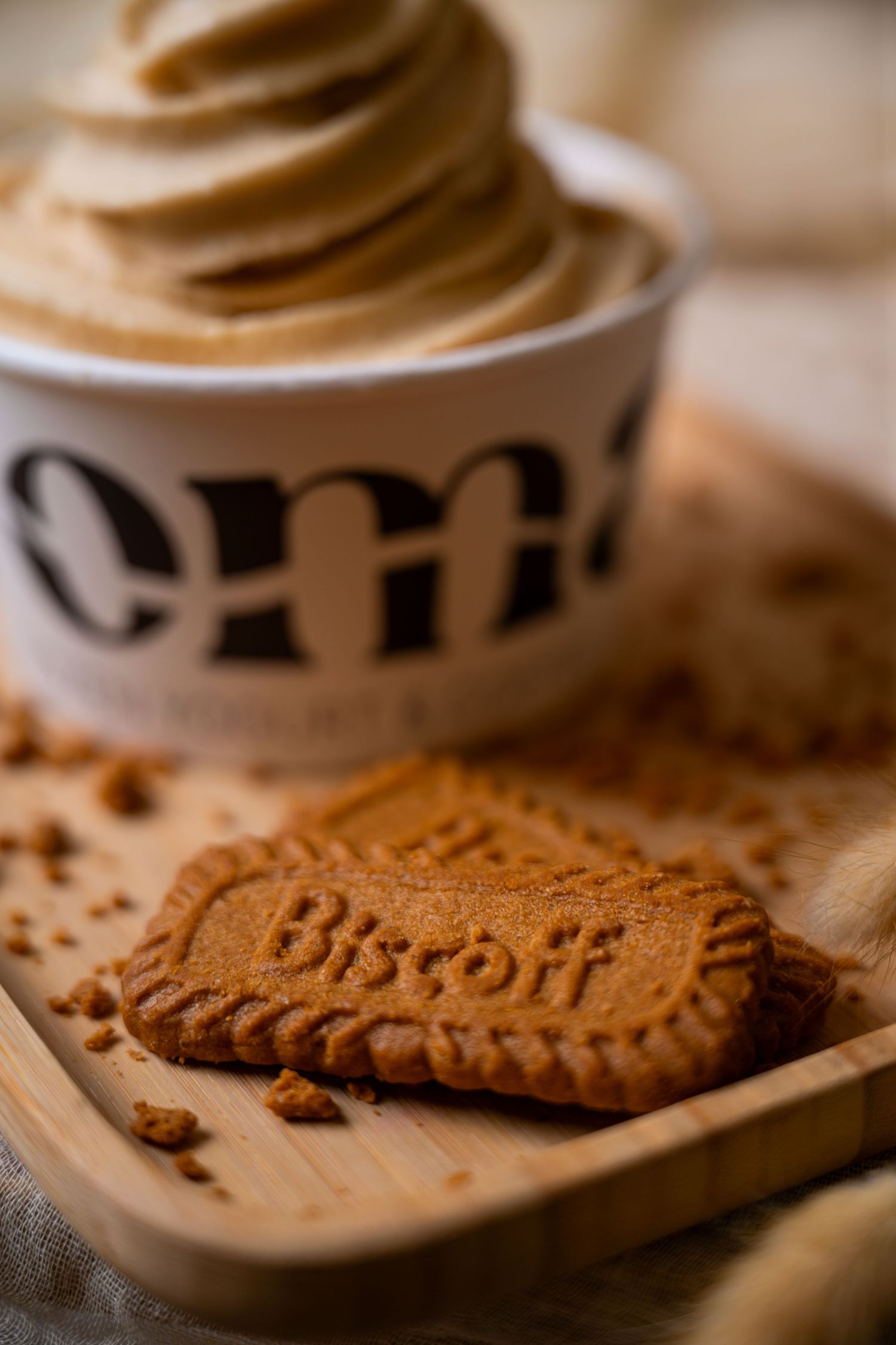 Biscoff cookie on wooden board beside creamy caramel soft serve ice cream in a white cup.
