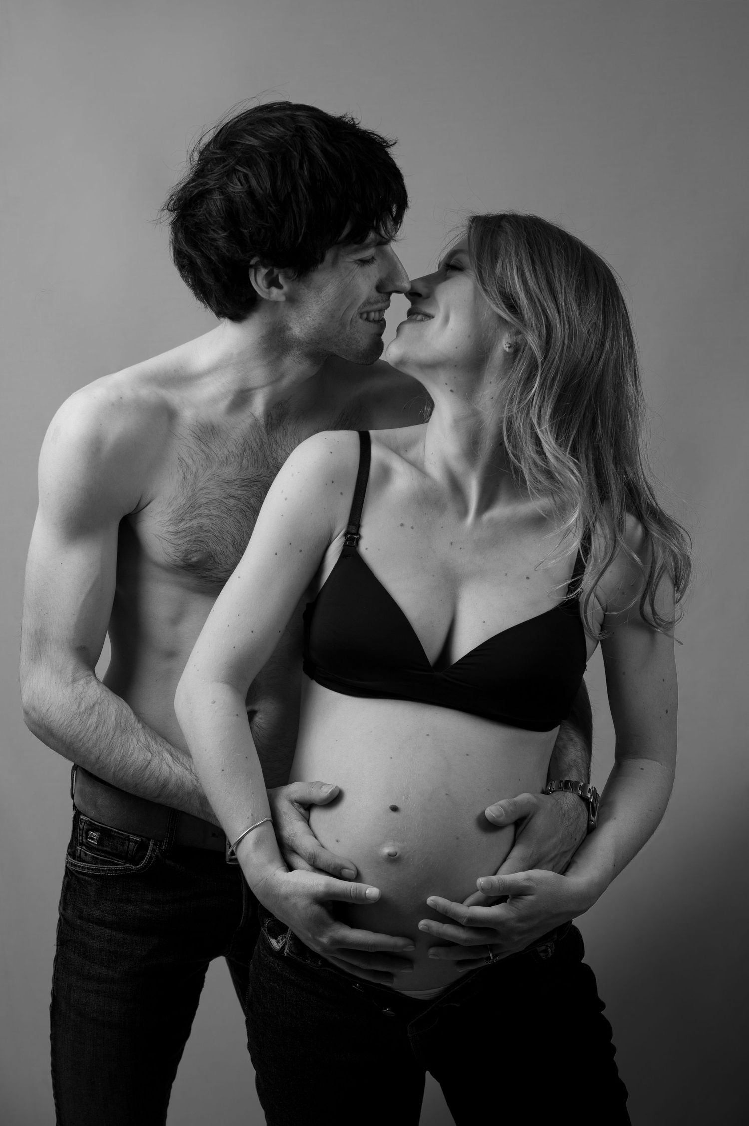 Black and white image of couple sharing a tender moment while cradling pregnant belly.