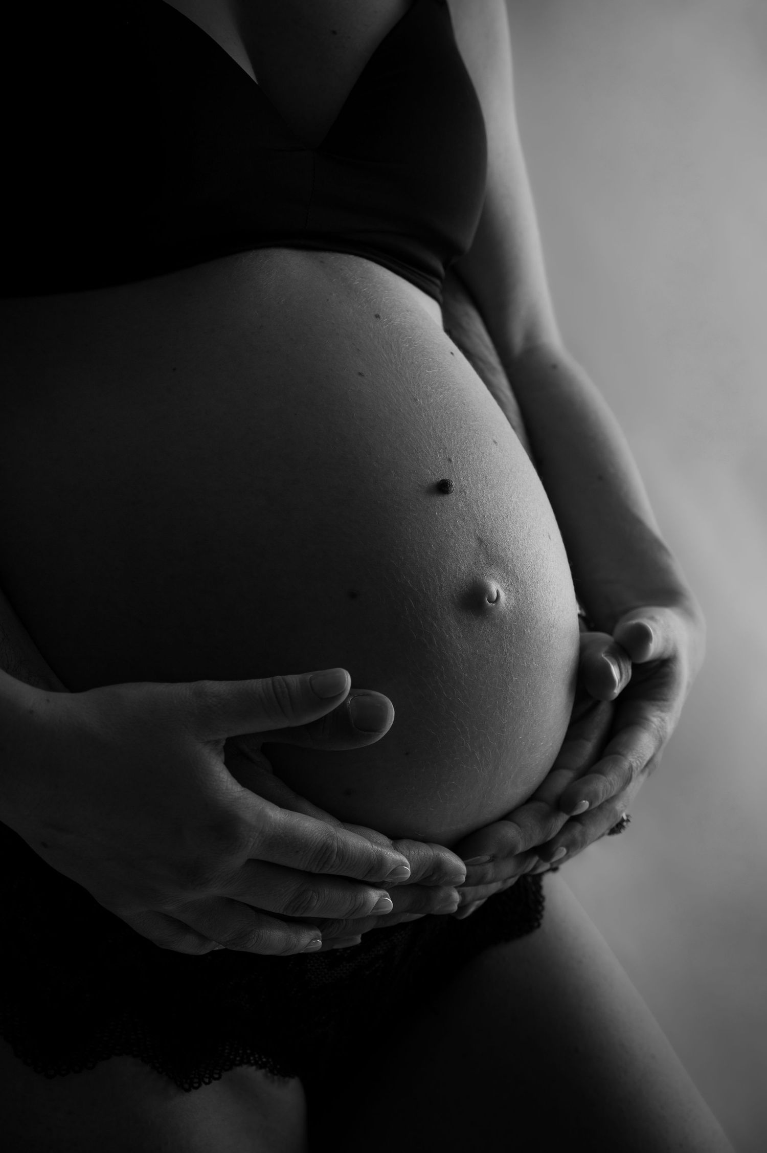 Close-up black and white photo of pregnant belly being gently held by two pairs of hands.