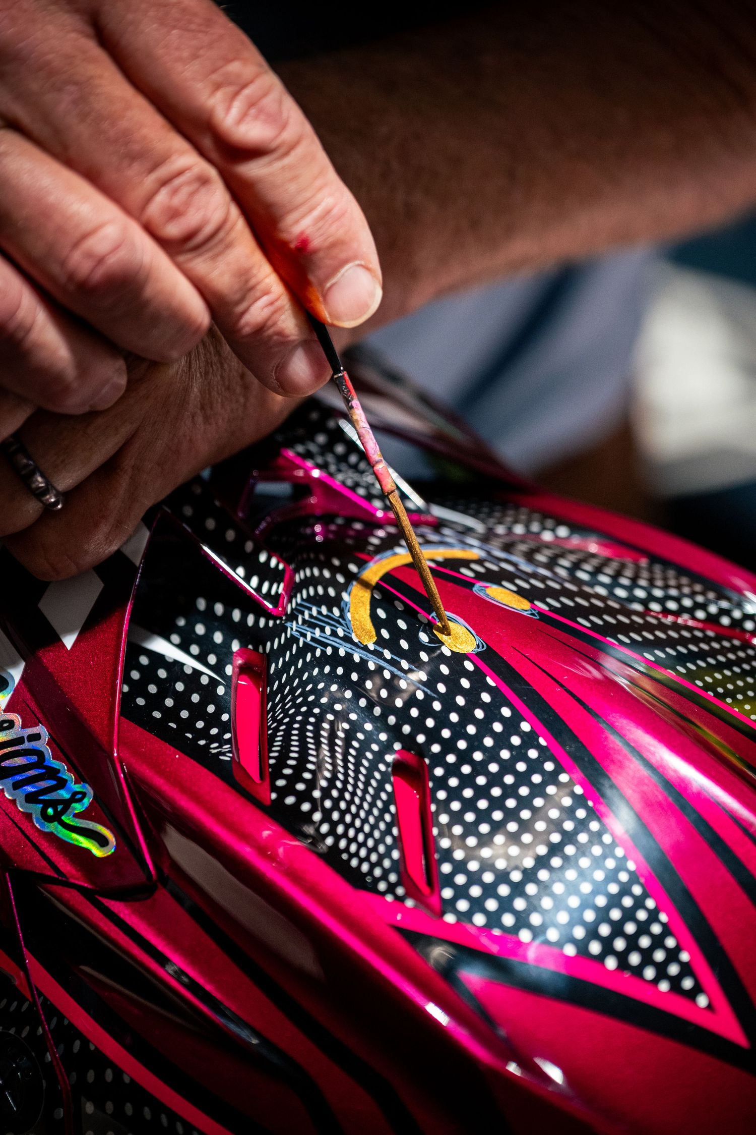 Artist hands detailing a colorful red and black polka dot motorcycle helmet with a brush.