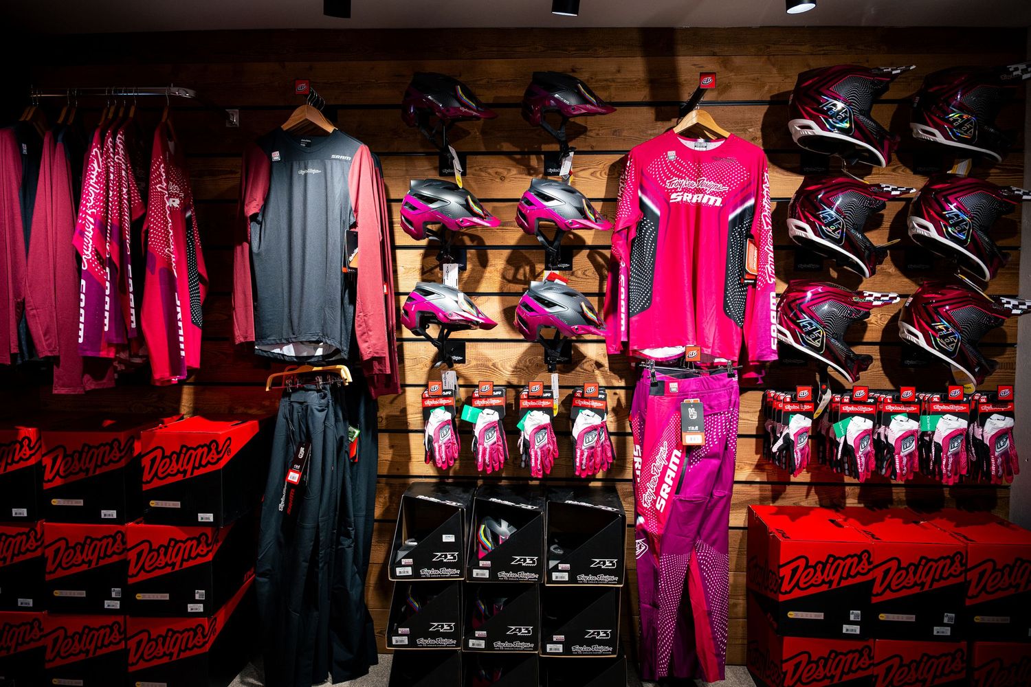 Pink and black motocross gear display including helmets, jerseys, and accessories in a retail store.